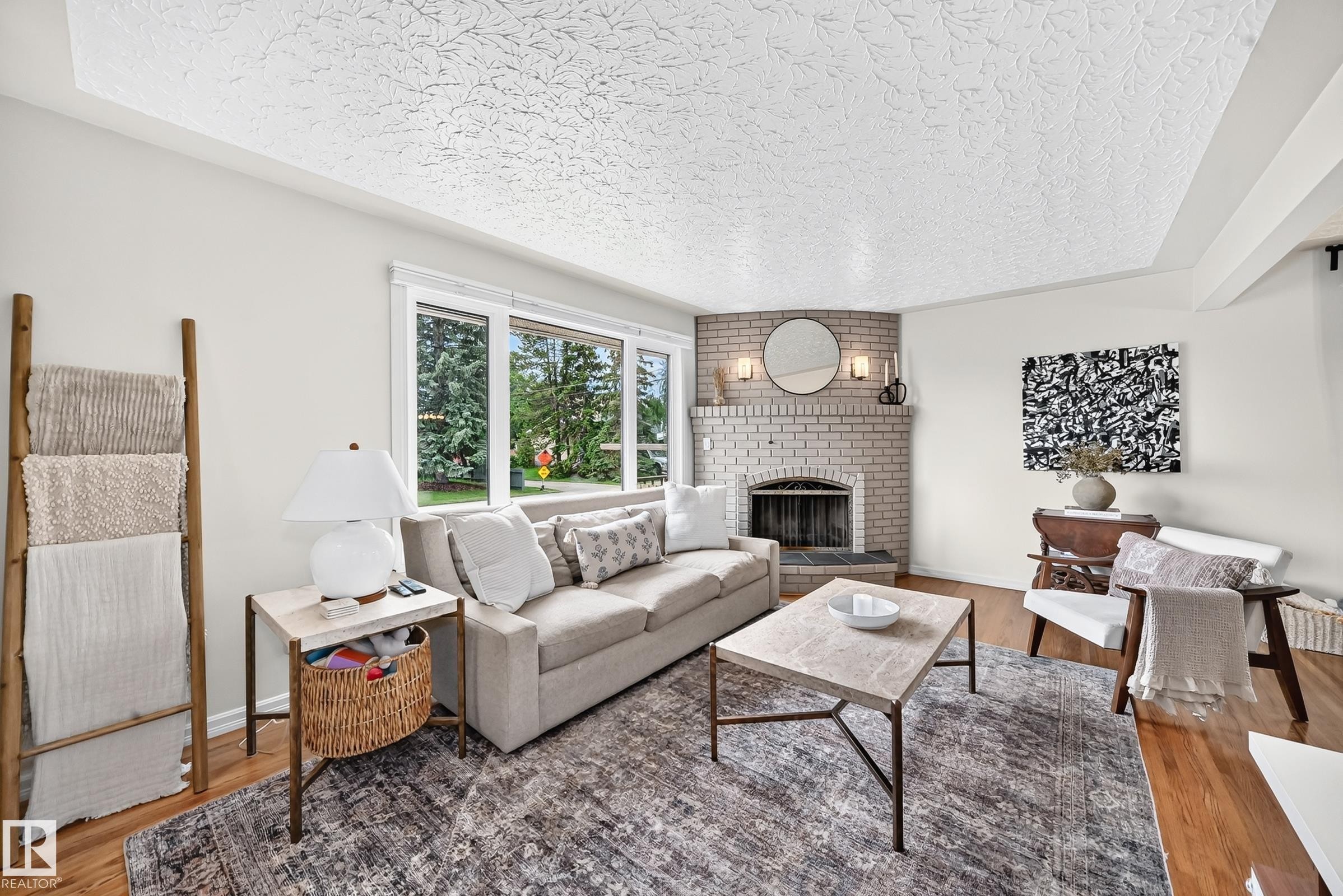 Recessed corner fireplace with a light brick surround, hardwood flooring, and large windows - 16406 87A Avenue Nw, Edmonton, AB - Indoor Photo Showing Living Room With Fireplace