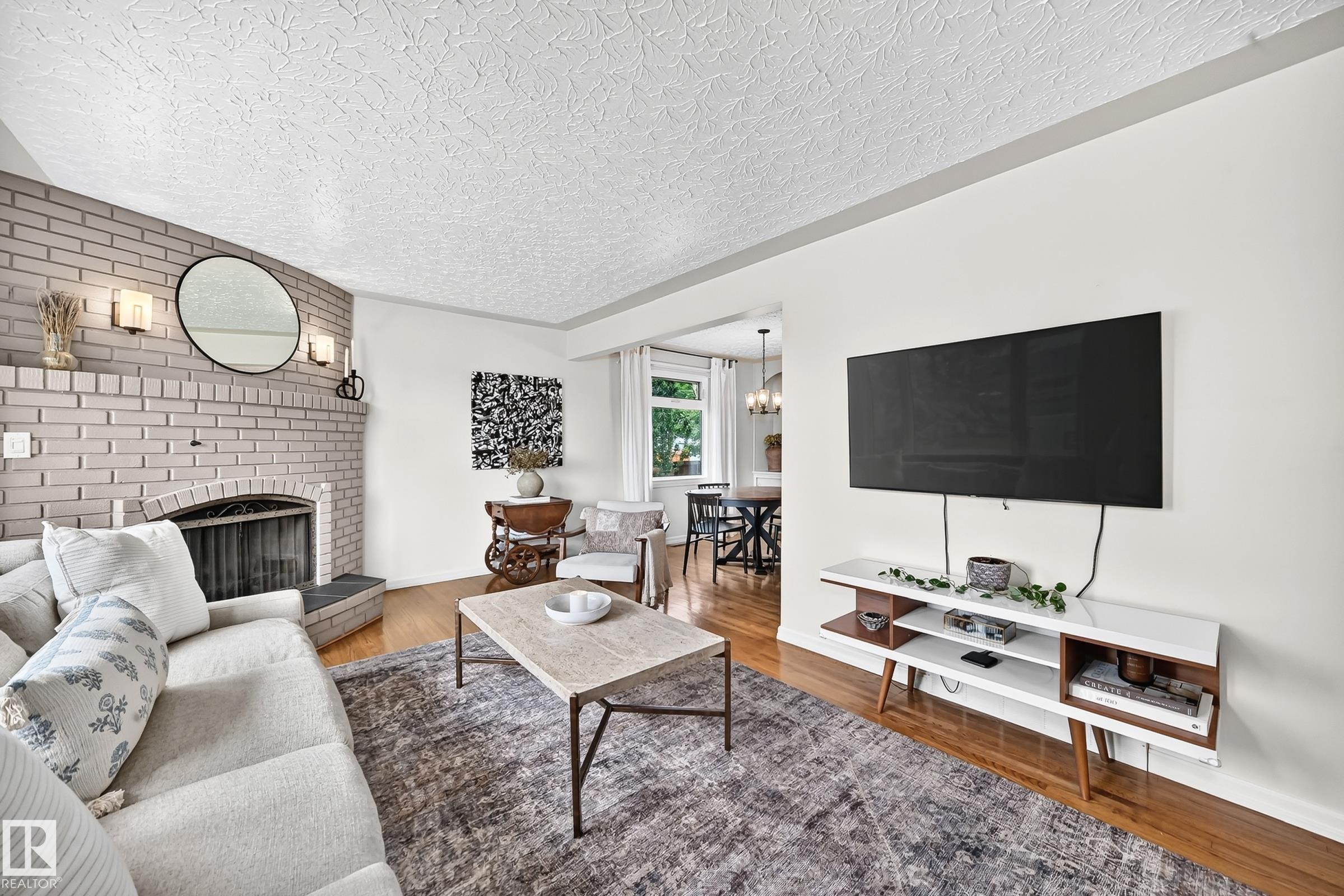 Brick fireplace with a metal grate and sconce lighting, wood-finish flooring, and white walls - 16406 87A Avenue Nw, Edmonton, AB - Indoor Photo Showing Living Room With Fireplace
