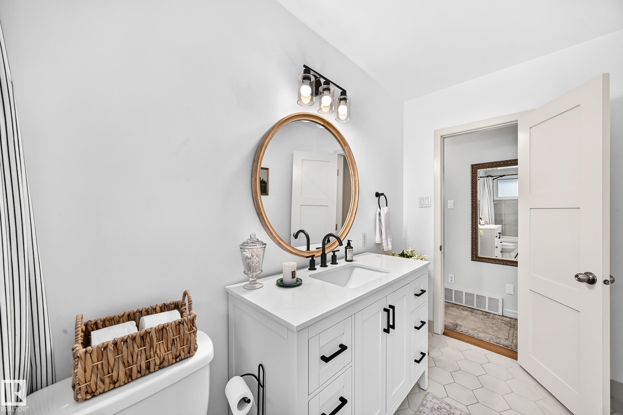 White vanity with dual integrated sinks, matte black hardware, and a gold-framed round mirror - 16406 87A Avenue Nw, Edmonton, AB - Indoor Photo Showing Bathroom