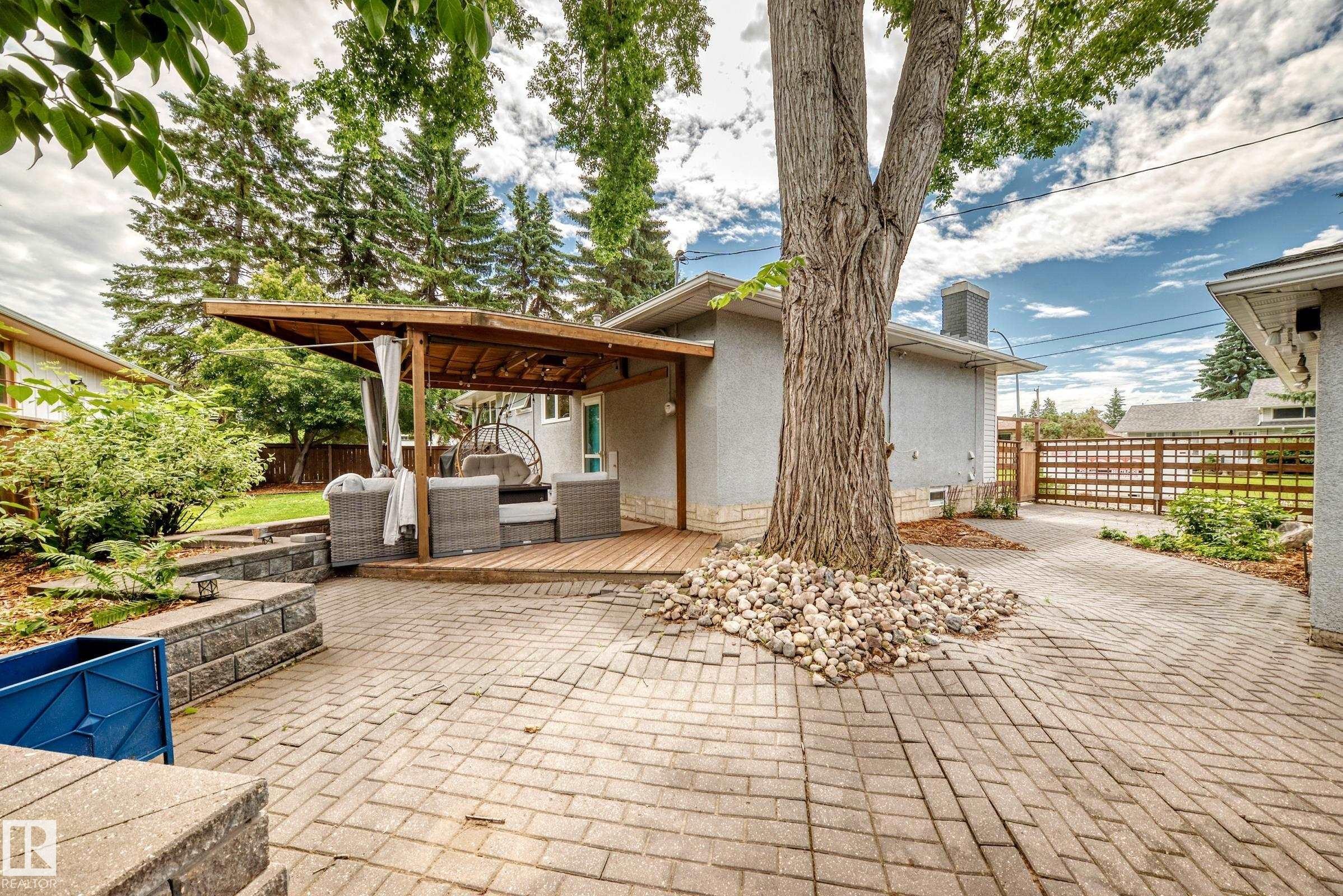 Paved patio with retaining wall, wooden deck, and a covered outdoor living space - 16406 87A Avenue Nw, Edmonton, AB - Outdoor With Deck Patio Veranda