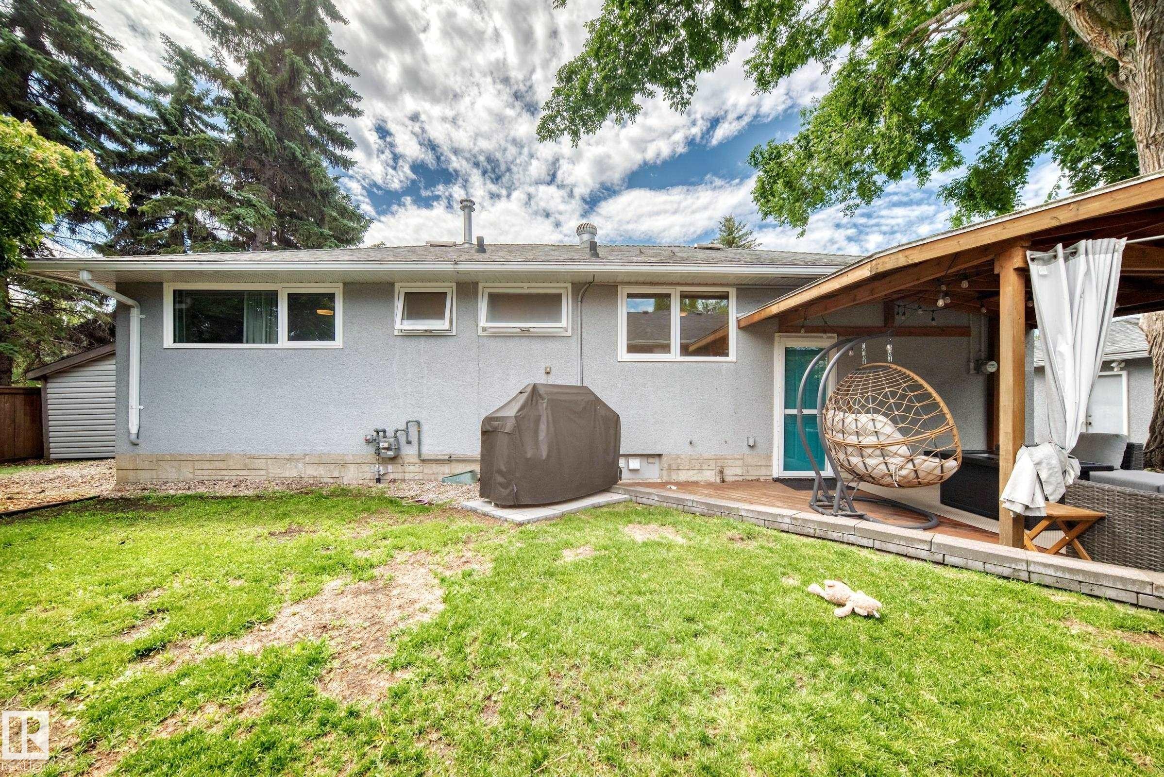 Expansive rear yard featuring green space, a wooden deck, and a covered patio area with exposed wood beams - 16406 87A Avenue Nw, Edmonton, AB - Outdoor