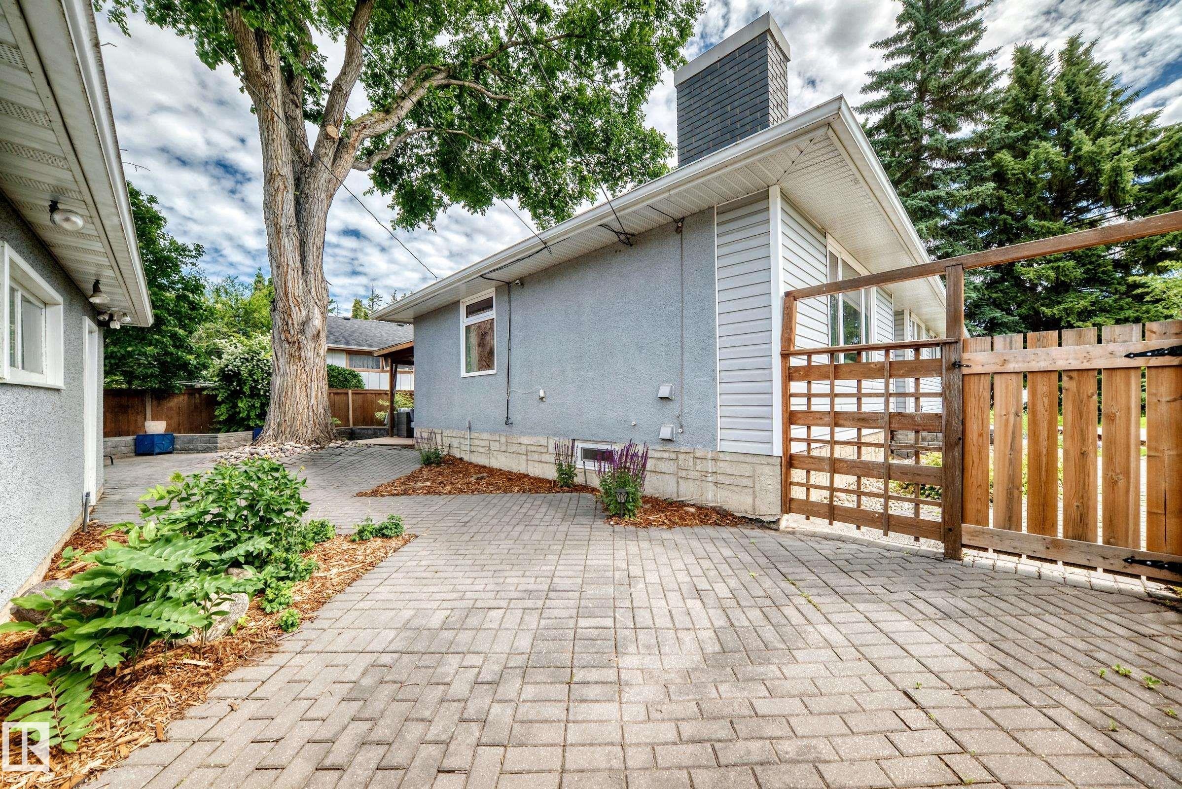 Paver stone driveway with a wooden privacy fence, mature trees, and landscaping elements - 16406 87A Avenue Nw, Edmonton, AB - Outdoor With Exterior