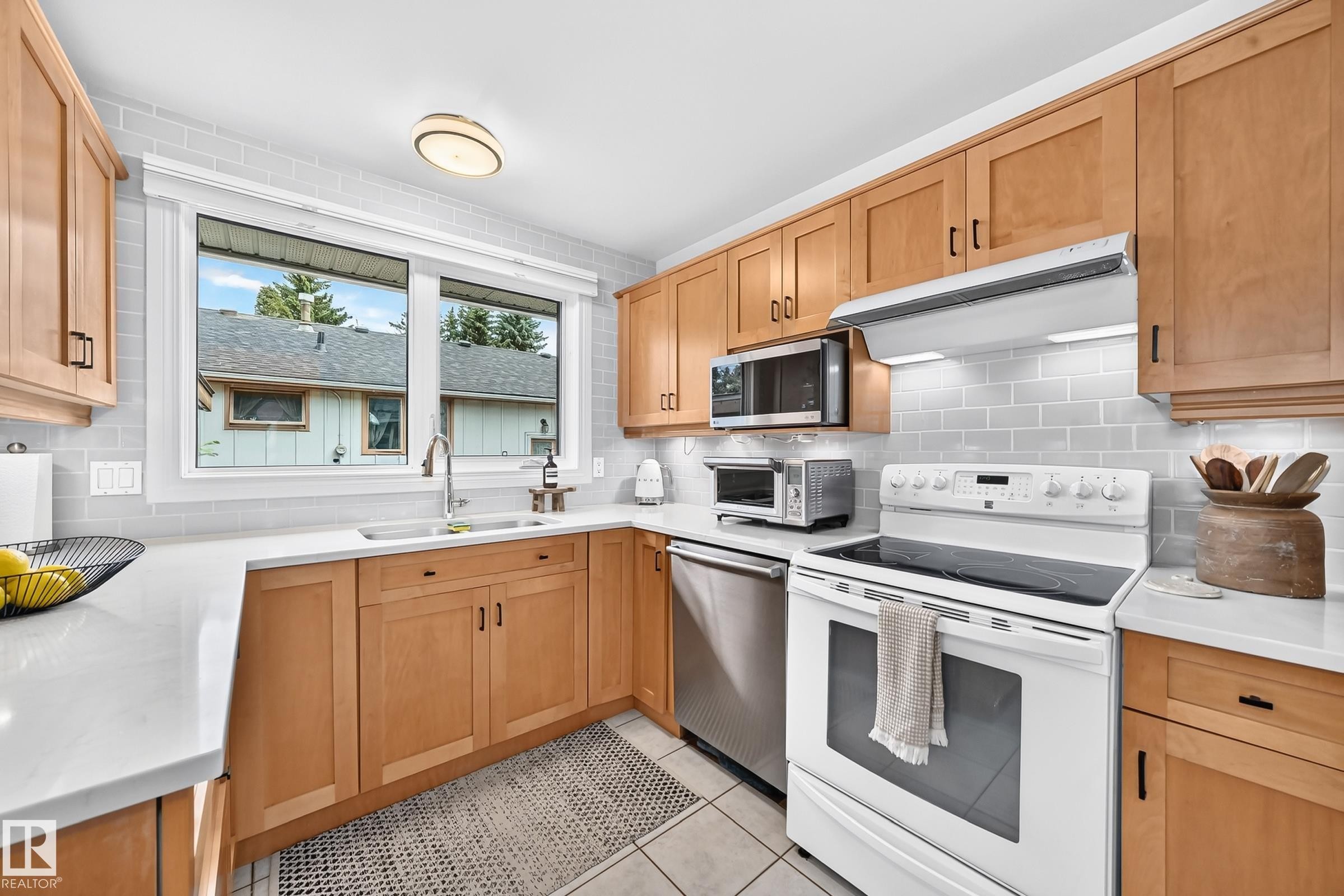 Kitchen featuring light wood-finish cabinetry, white countertops, tile flooring, subway tile backsplash, and a stainless steel dishwasher - 16406 87A Avenue Nw, Edmonton, AB - Indoor Photo Showing Kitchen With Double Sink