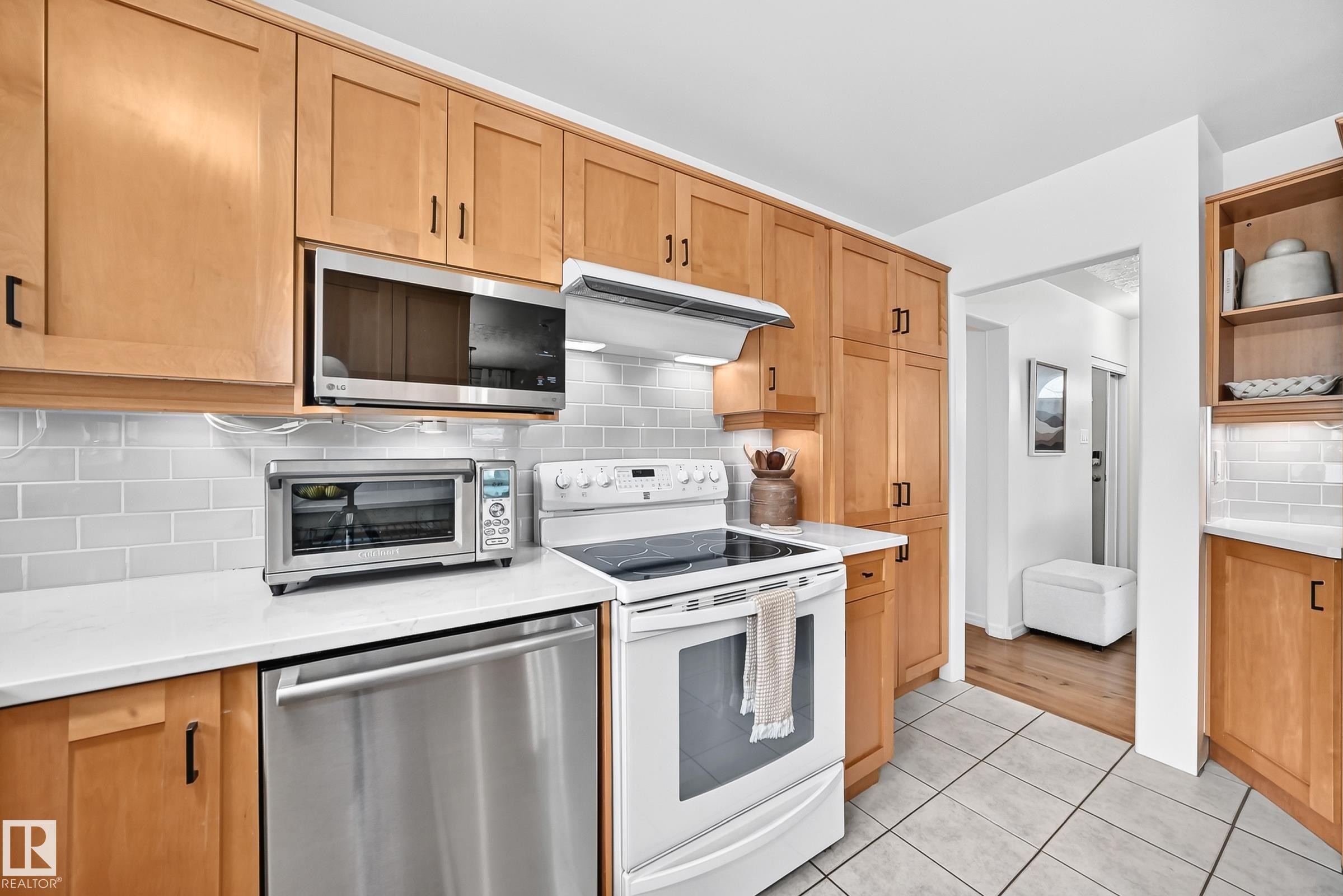 Light wood-finish cabinetry, white countertops, subway tile backsplash, white electric range, and stainless steel dishwasher - 16406 87A Avenue Nw, Edmonton, AB - Indoor Photo Showing Kitchen