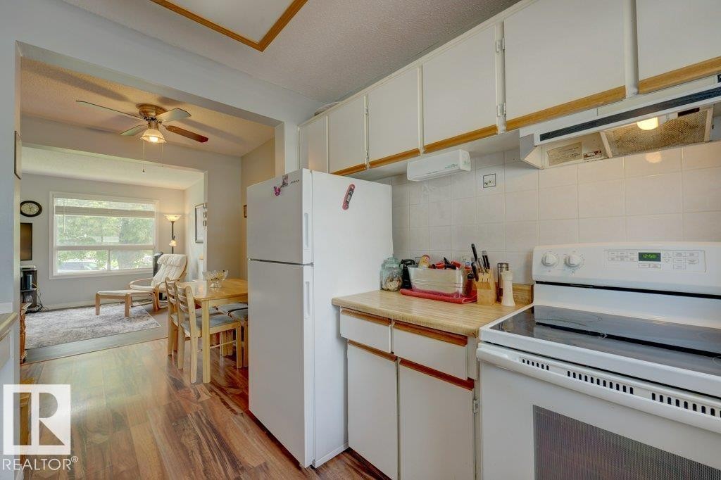 Wood-finish flooring, white upper and lower cabinetry, white tile backsplash, and a white electric range - 307 Northgate Terrace Nw, Edmonton, AB - Indoor Photo Showing Kitchen