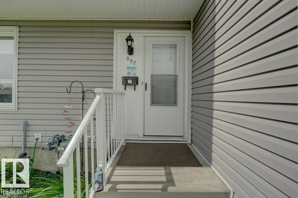 Gray horizontal siding with a white entry door, an exterior wall light fixture, and white porch railings - 307 Northgate Terrace Nw, Edmonton, AB - Outdoor With Exterior