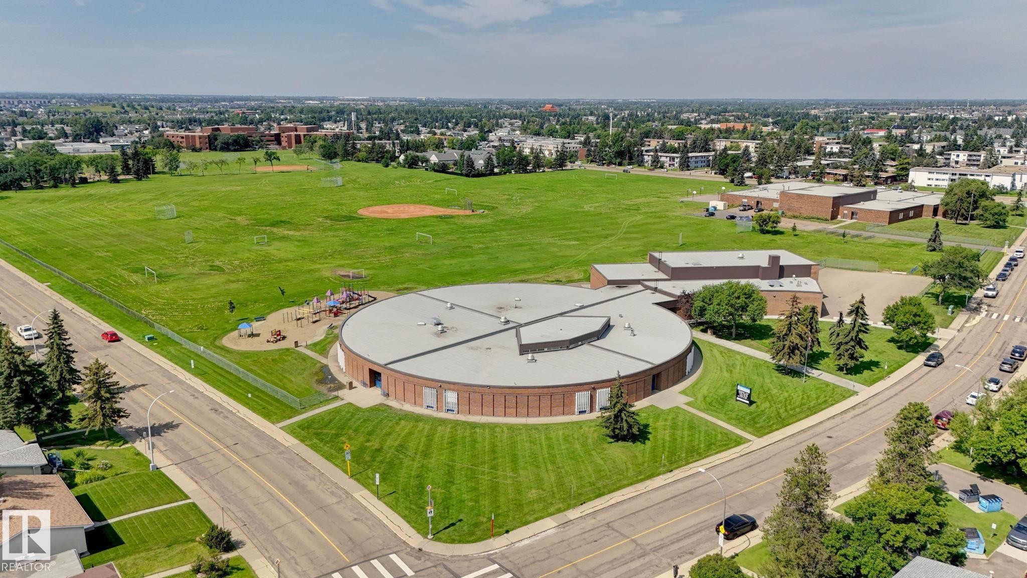 Circular brick building with a large adjacent green space featuring multiple sports fields and a playground area - 307 Northgate Terrace Nw, Edmonton, AB - Outdoor With View
