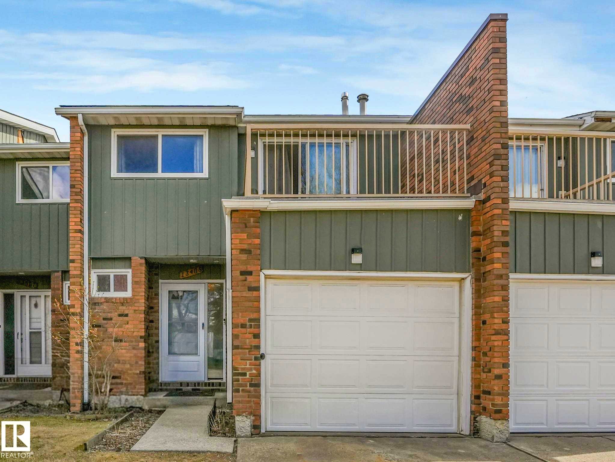 Townhome exterior featuring a white garage door, brick accents, and a second-story balcony with railings - 13405 40 St Nw, Edmonton, AB - Outdoor