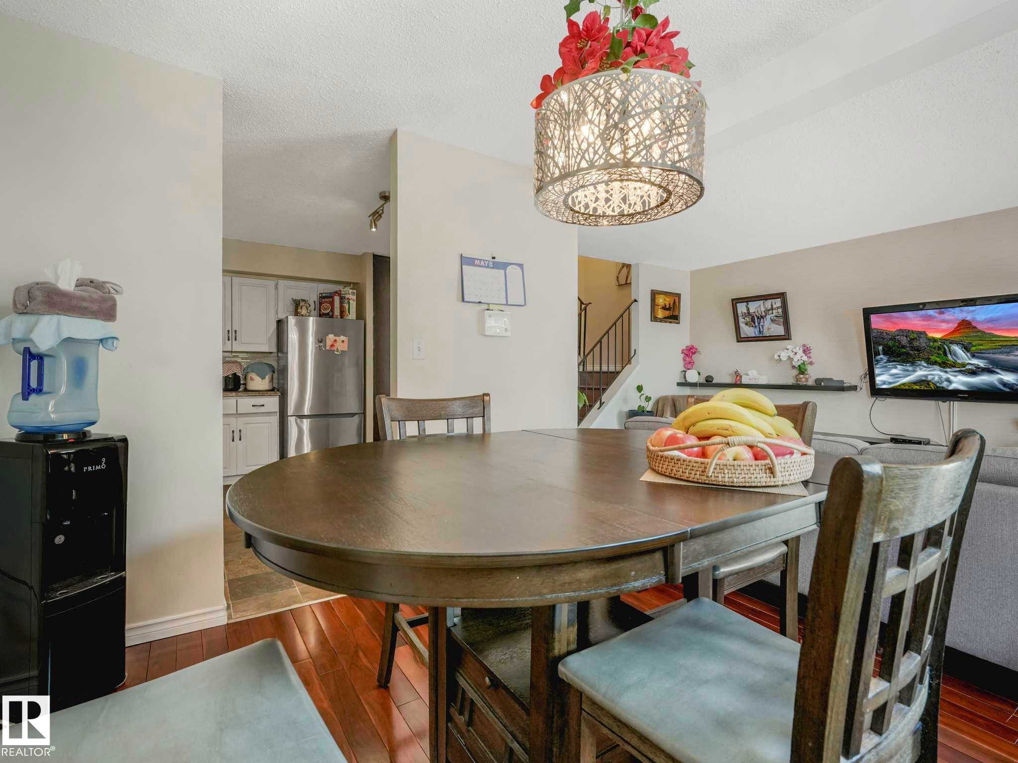 Dining area featuring wood-finish flooring, a contemporary drum pendant light, and a wooden dining table with chairs - 13405 40 St Nw, Edmonton, AB - Indoor Photo Showing Dining Room