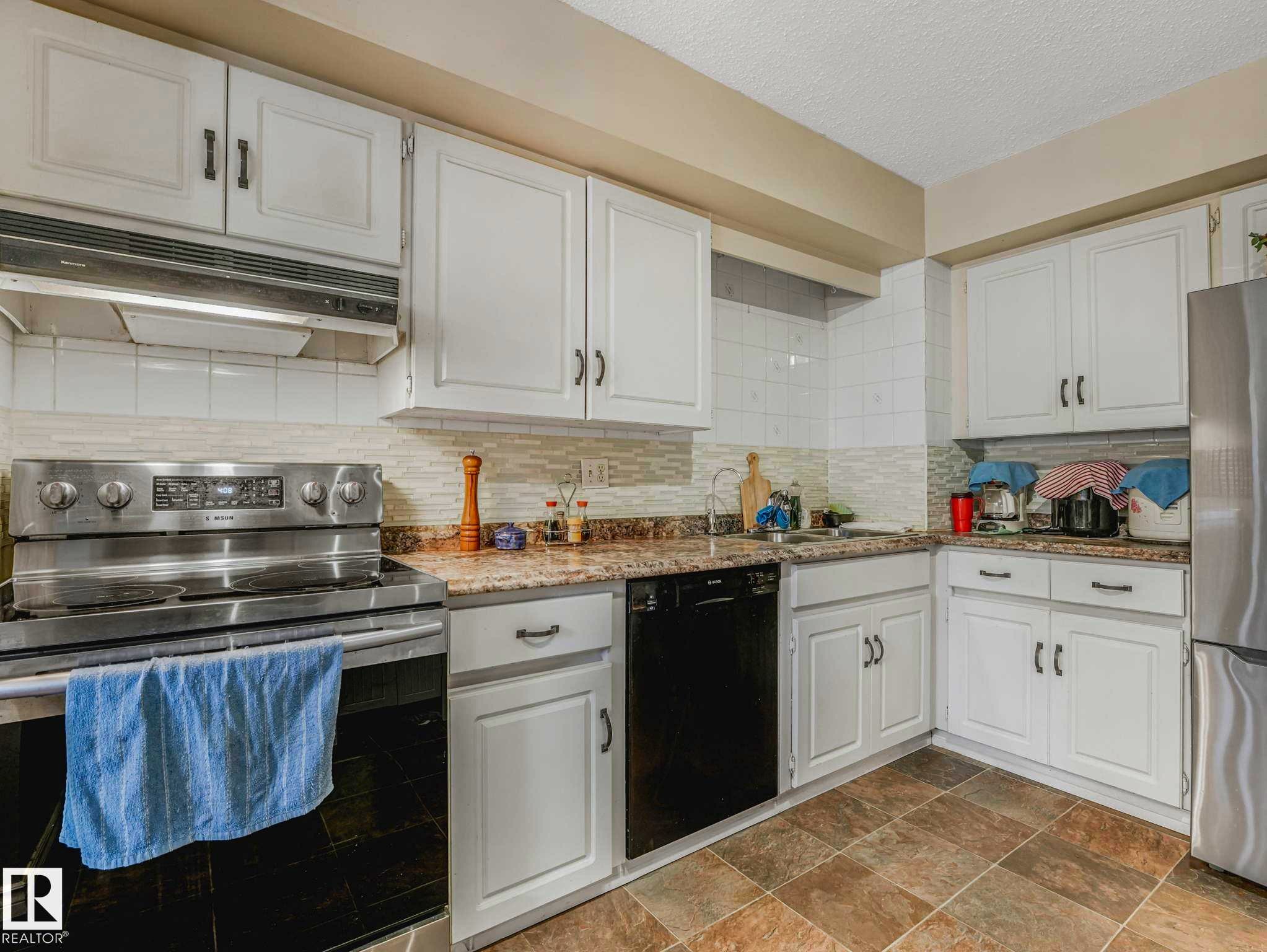 Kitchen featuring white shaker-style cabinetry, a stainless steel range, and a tile backsplash - 13405 40 St Nw, Edmonton, AB - Indoor Photo Showing Kitchen