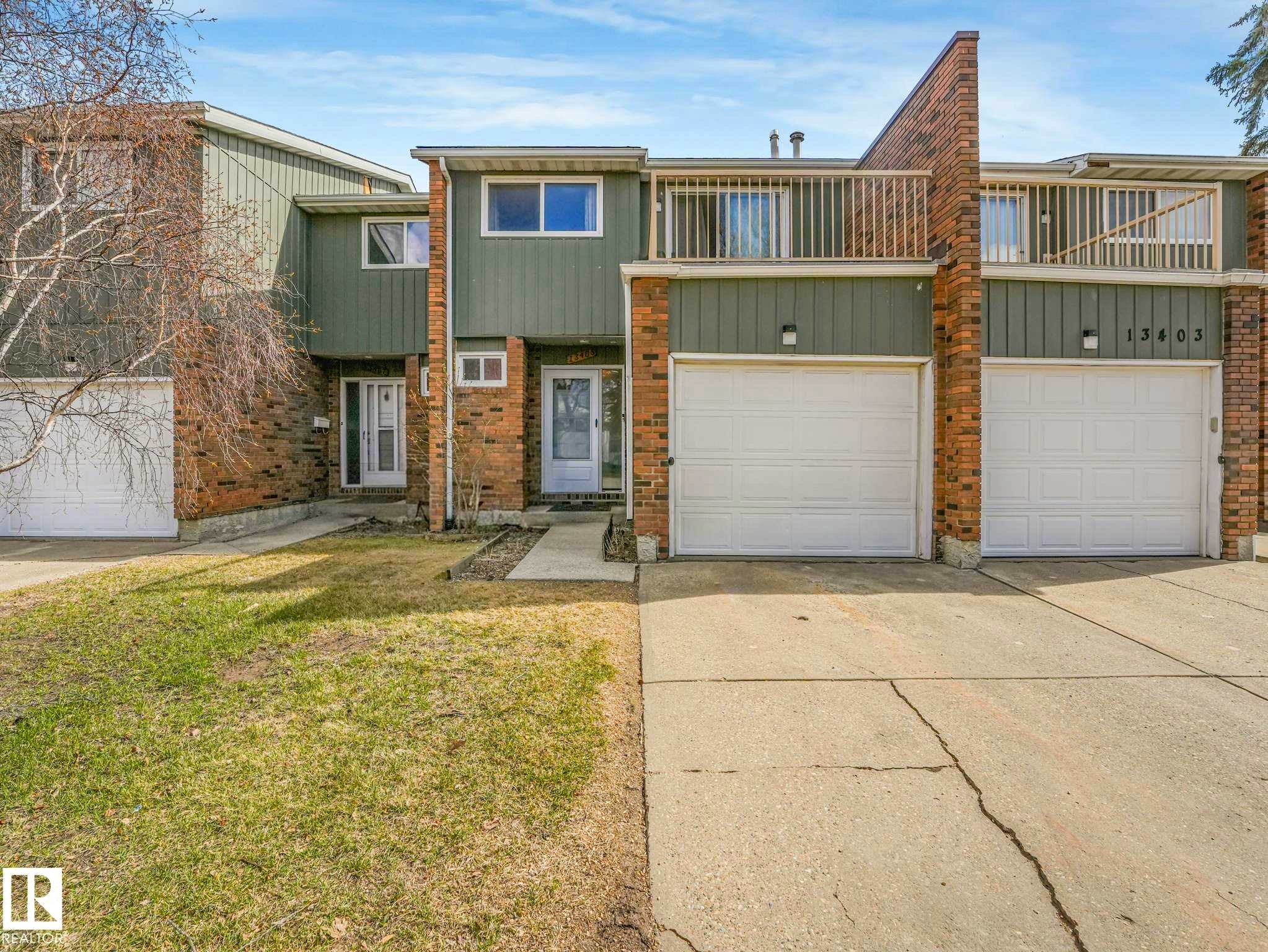 Townhome exterior featuring brick and vertical siding, attached garage, concrete driveway, and front entryway - 13405 40 St Nw, Edmonton, AB - Outdoor