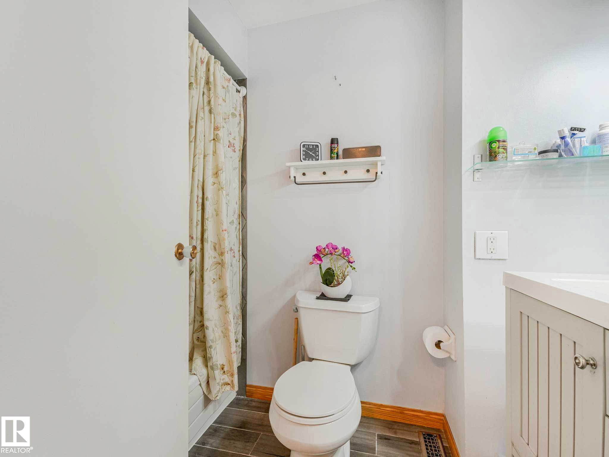 Bathroom featuring a white toilet, wood-finish flooring, a white vanity with paneling and a light-colored countertop, and a shower area - 13405 40 St Nw, Edmonton, AB - Indoor Photo Showing Bathroom