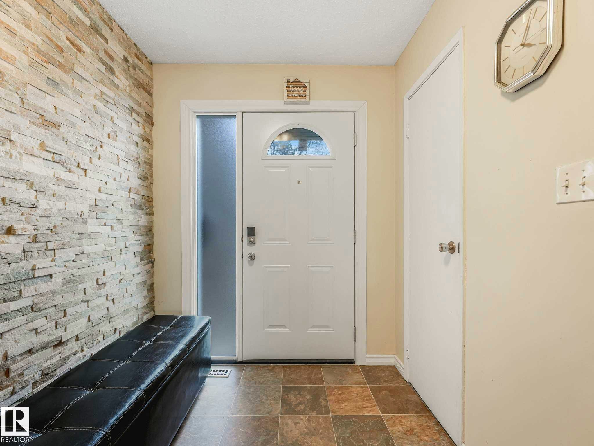 Foyer featuring a stone veneer accent wall, tiled flooring, and a white entry door with an arched window insert and frosted glass sidelight - 13405 40 St Nw, Edmonton, AB - Indoor Photo Showing Other Room