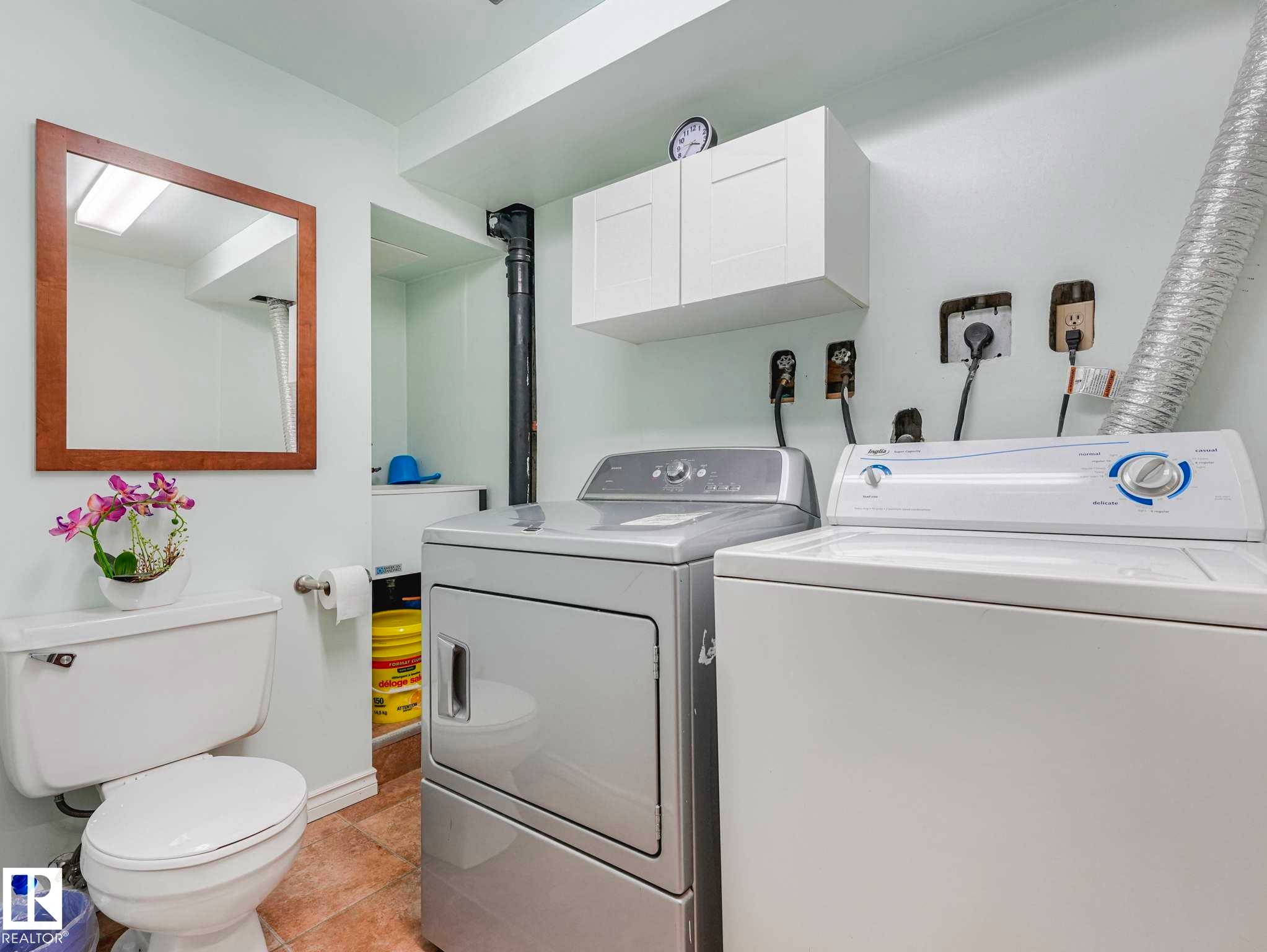 Laundry area with a white washing machine, stacked dryer, and overhead white cabinetry - 13405 40 St Nw, Edmonton, AB - Indoor Photo Showing Laundry Room
