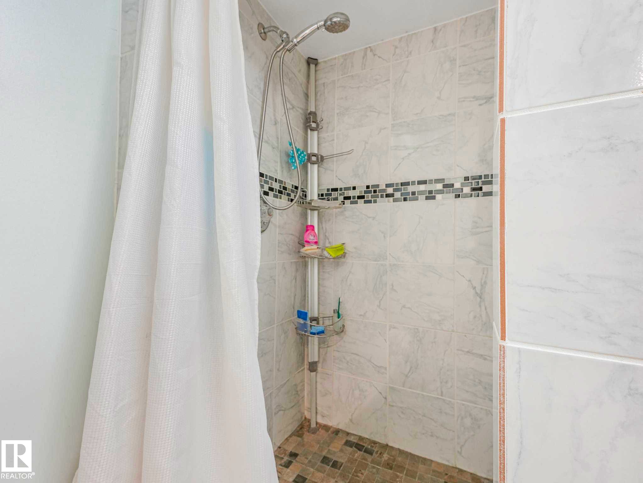 Shower enclosure featuring light-toned large format wall tiling, a decorative glass mosaic accent band, and a mosaic tile shower pan - 13405 40 St Nw, Edmonton, AB - Indoor Photo Showing Bathroom