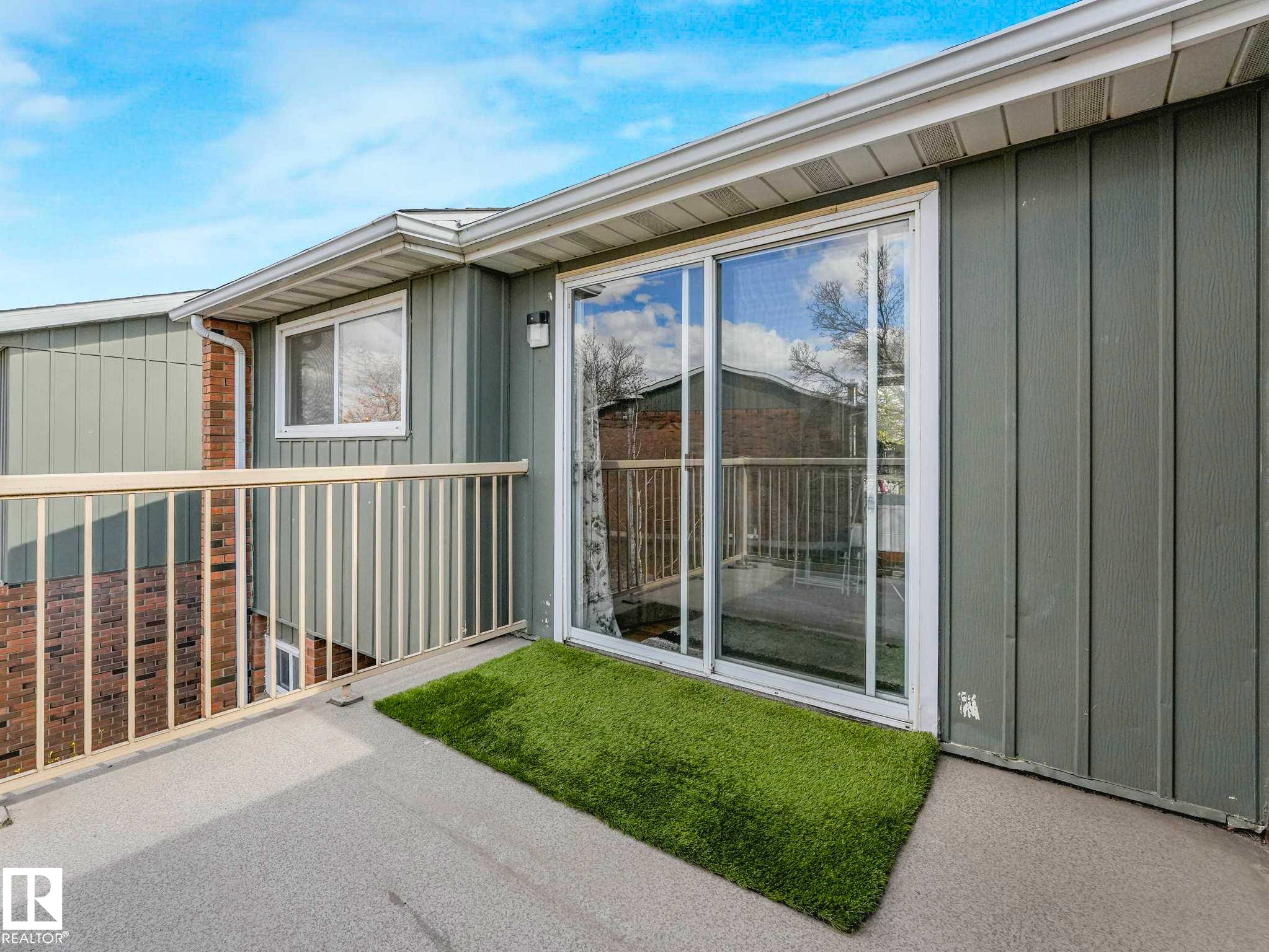 Outdoor balcony featuring concrete flooring, a sliding glass door, white railing, and exterior wall paneling - 13405 40 St Nw, Edmonton, AB - Outdoor With Exterior