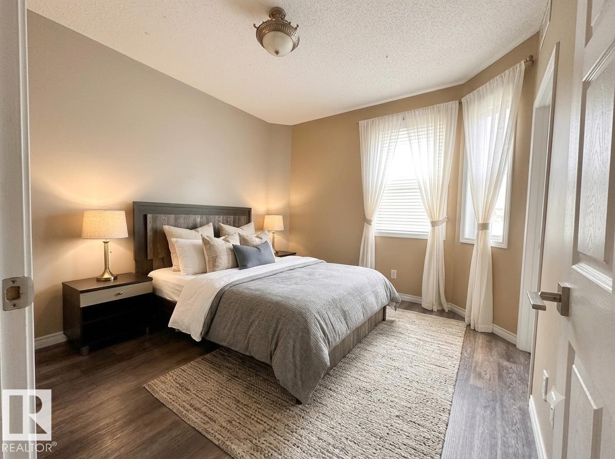 Warm neutral wall tones, wood-finish flooring, two large windows, and a classic ceiling fixture - #103 8108 109 St Nw, Edmonton, AB - Indoor Photo Showing Bedroom