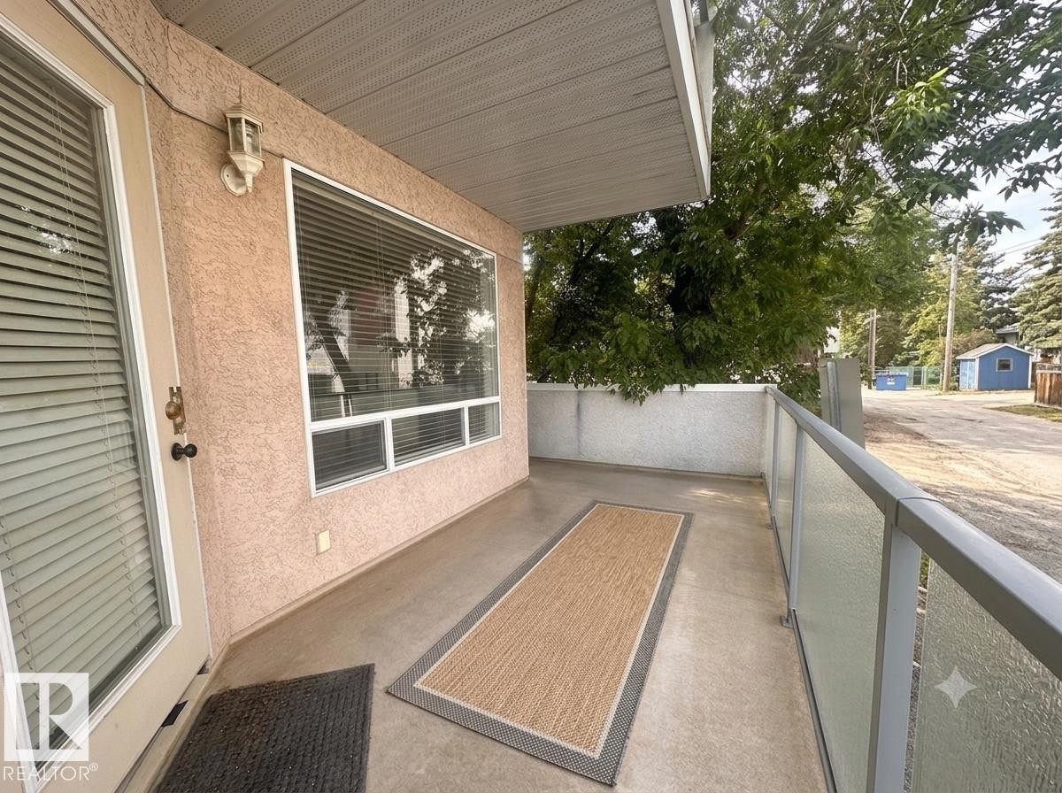 Private balcony featuring a glass panel railing, concrete flooring, and an exterior wall light - #103 8108 109 St Nw, Edmonton, AB - Outdoor With Balcony With Exterior