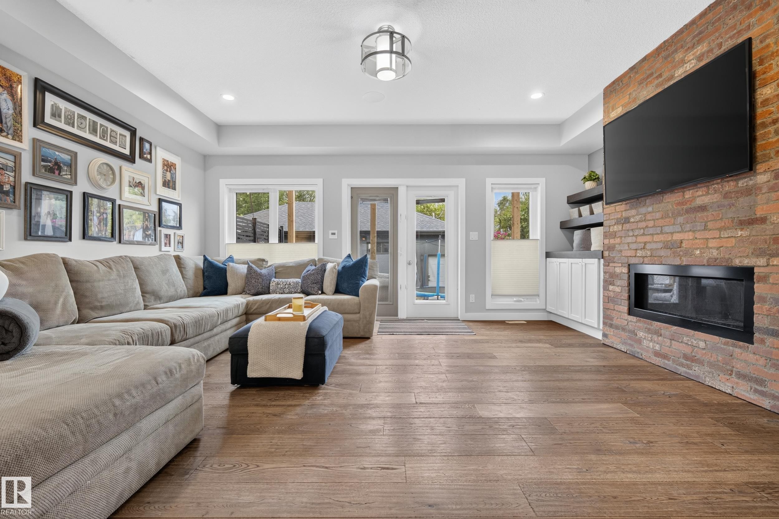 Expansive wood-finish flooring, recessed lighting, and a brick-finish fireplace - 11018 122 Street Nw, Edmonton, AB - Indoor Photo Showing Living Room With Fireplace