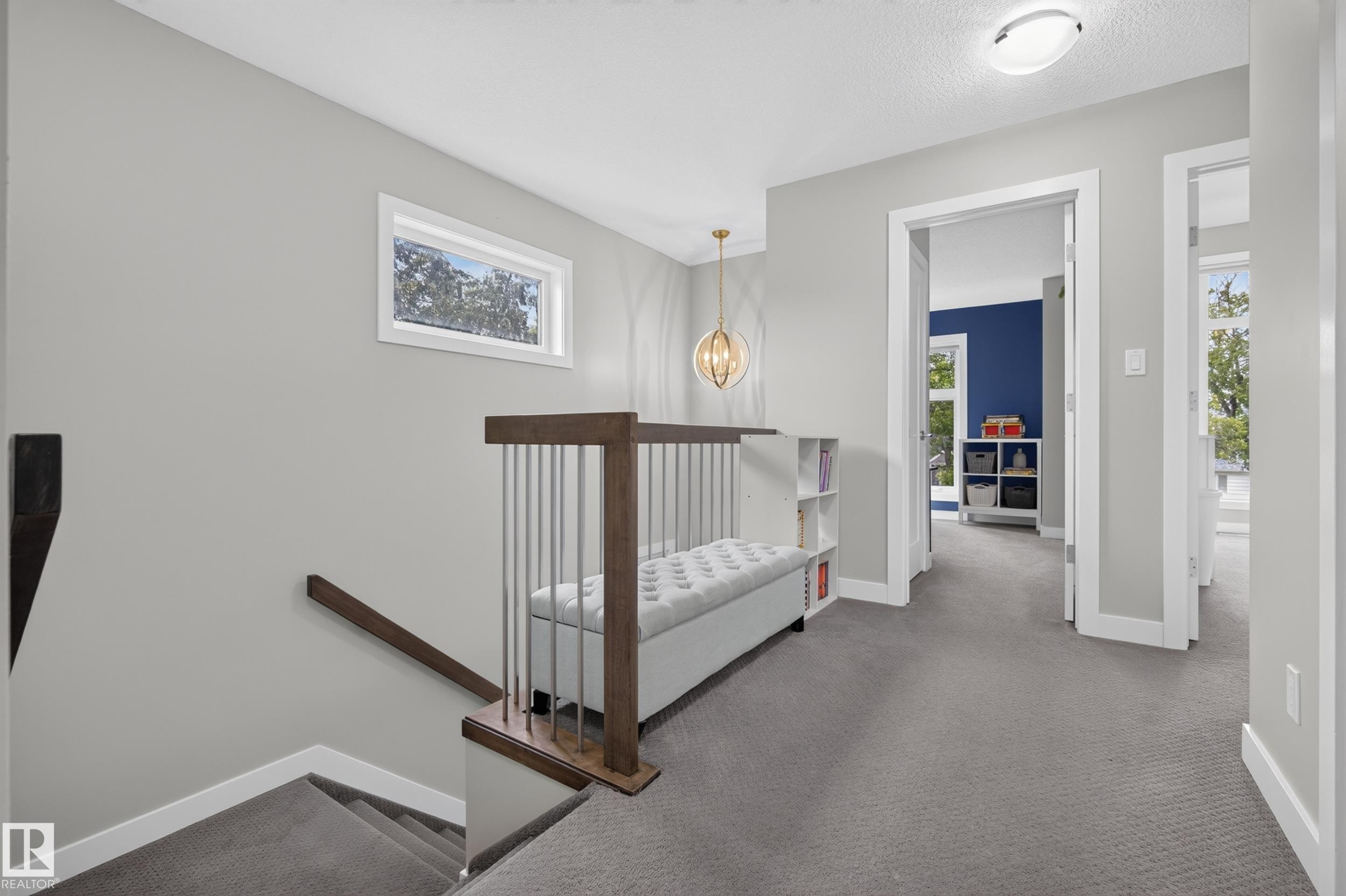 Carpeted upper landing with a contemporary open railing, built-in bench, and a modern chandelier - 11018 122 Street Nw, Edmonton, AB - Indoor