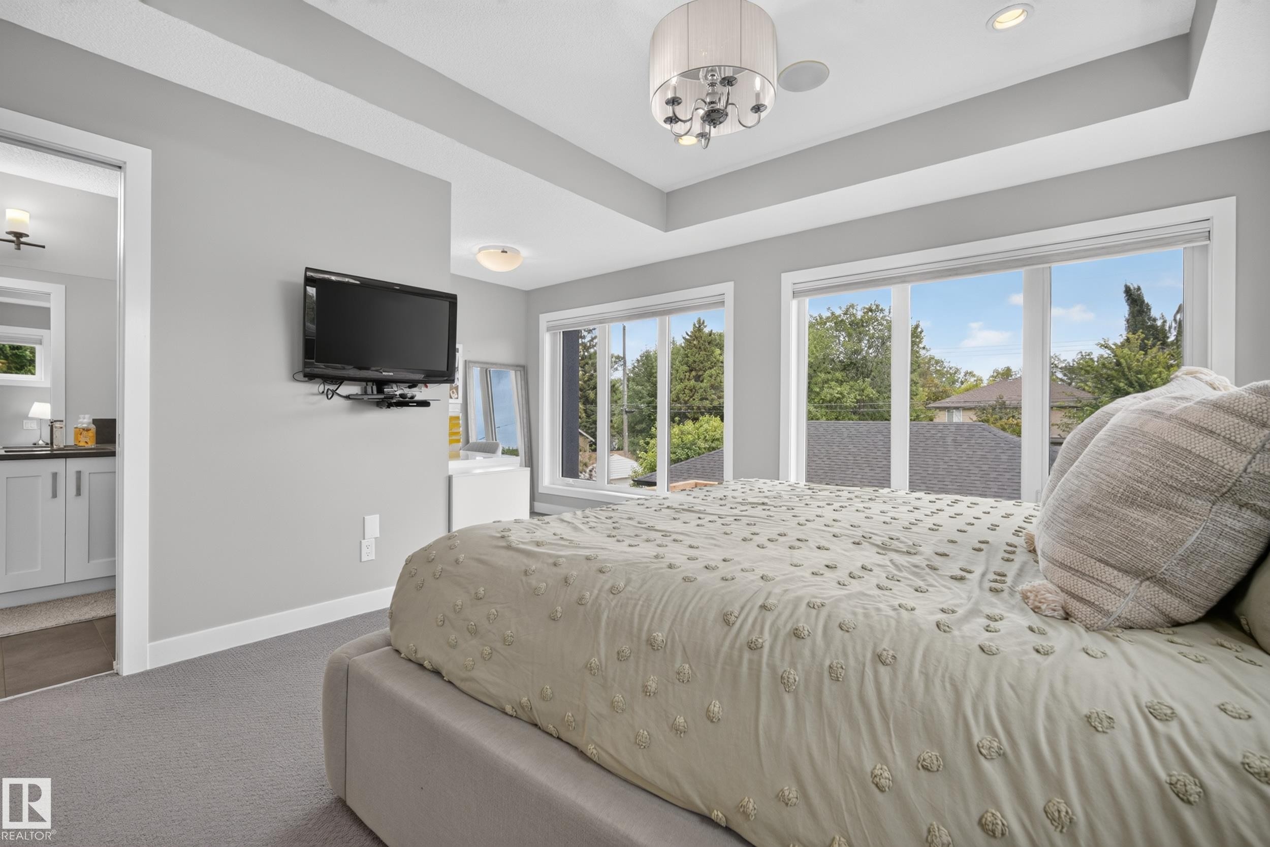 Recessed tray ceiling with a contemporary chandelier, multiple windows with roller shades, and plush carpeting - 11018 122 Street Nw, Edmonton, AB - Indoor Photo Showing Bedroom