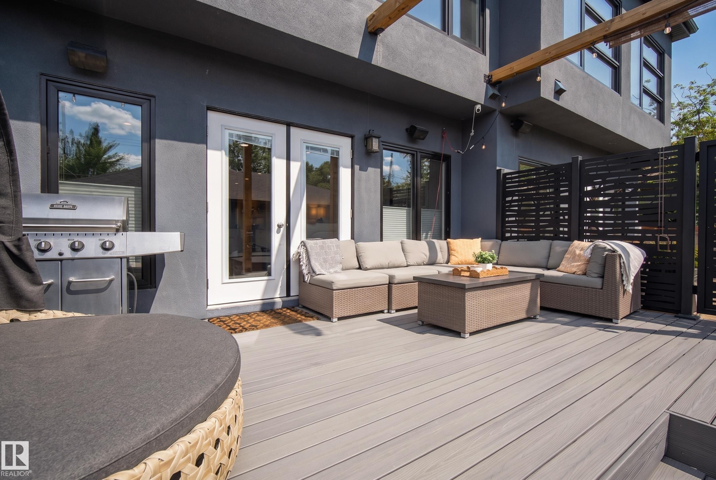 Expansive outdoor deck featuring wood-finish decking, a stucco exterior, and black-framed windows - 11018 122 Street Nw, Edmonton, AB - Outdoor With Deck Patio Veranda With Exterior