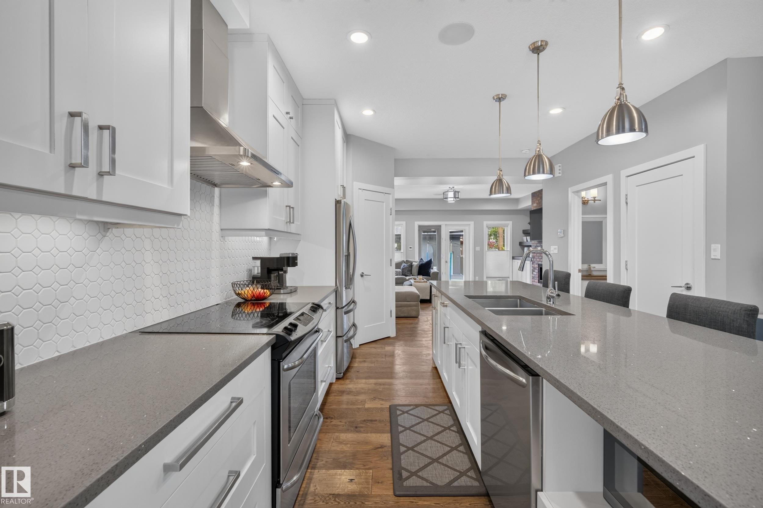 Kitchen featuring white shaker cabinetry, stainless steel appliances, a tile backsplash, wood-finish flooring, and a large center island with pendant lighting - 11018 122 Street Nw, Edmonton, AB - Indoor Photo Showing Kitchen With Double Sink With Upgraded Kitchen