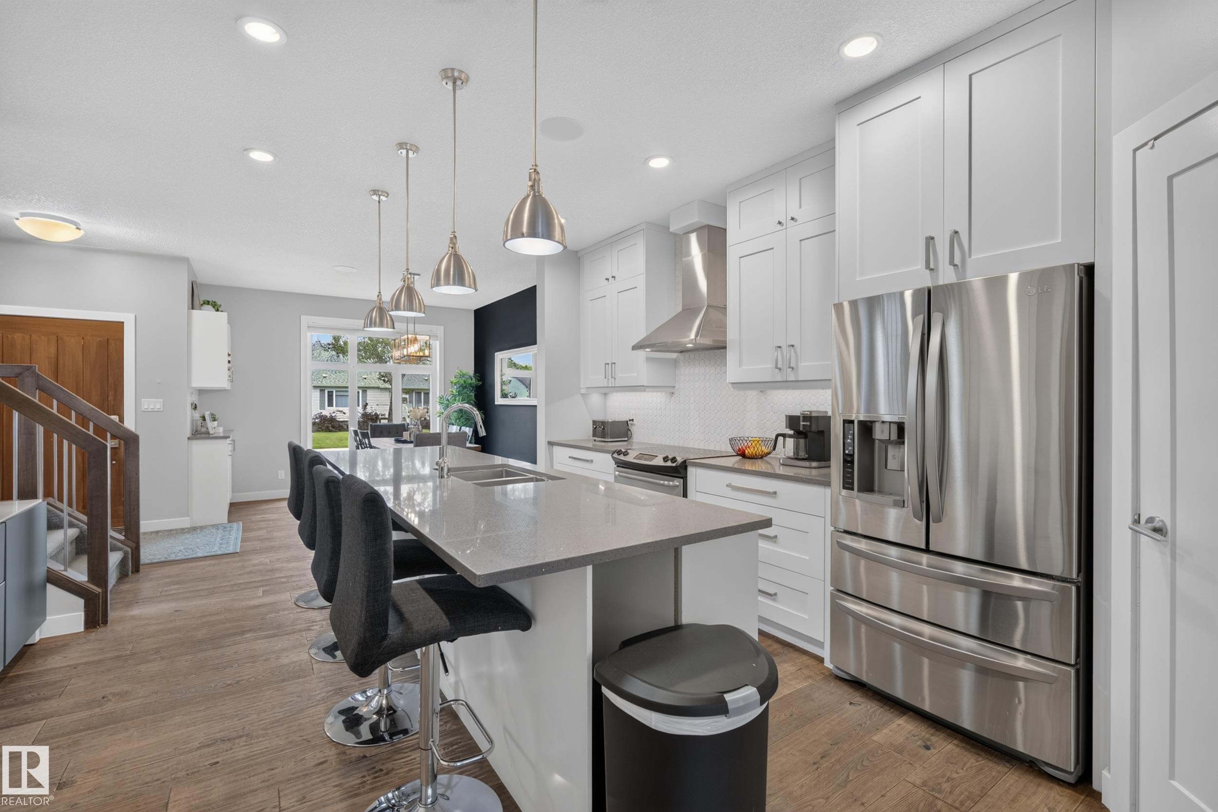 Kitchen featuring a large island with an undermount sink, pendant lighting, stainless steel appliances, white cabinetry, and wood-finish flooring - 11018 122 Street Nw, Edmonton, AB - Indoor Photo Showing Kitchen With Stainless Steel Kitchen With Upgraded Kitchen