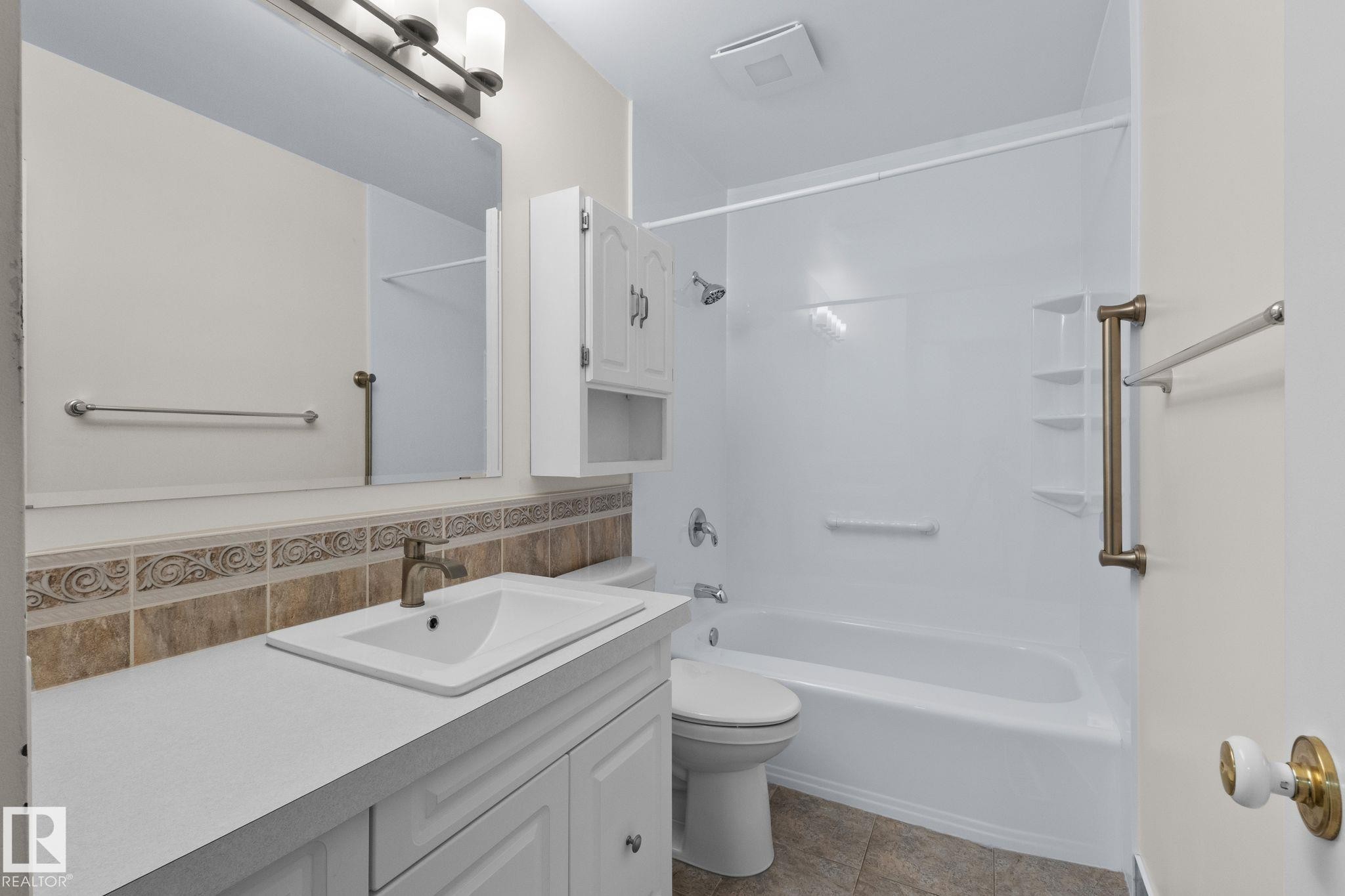 White vanity with a single basin sink, bronze-finish faucet, and a large wall-mounted mirror - 152 Woodstock Nw, Edmonton, AB - Indoor Photo Showing Bathroom