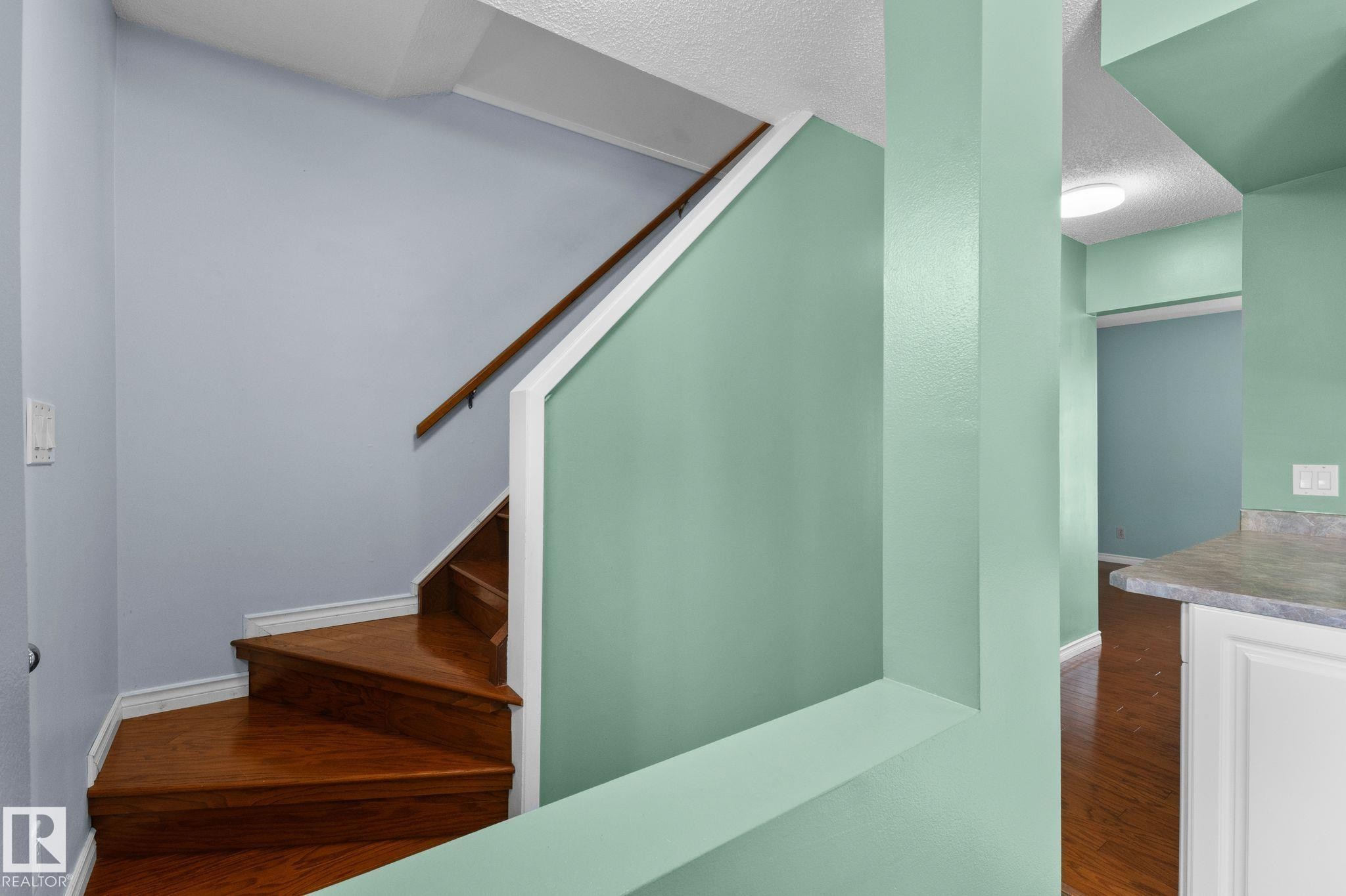 Hardwood staircase with a wood handrail, light-toned walls, and a built-in counter - 152 Woodstock Nw, Edmonton, AB - Indoor Photo Showing Other Room