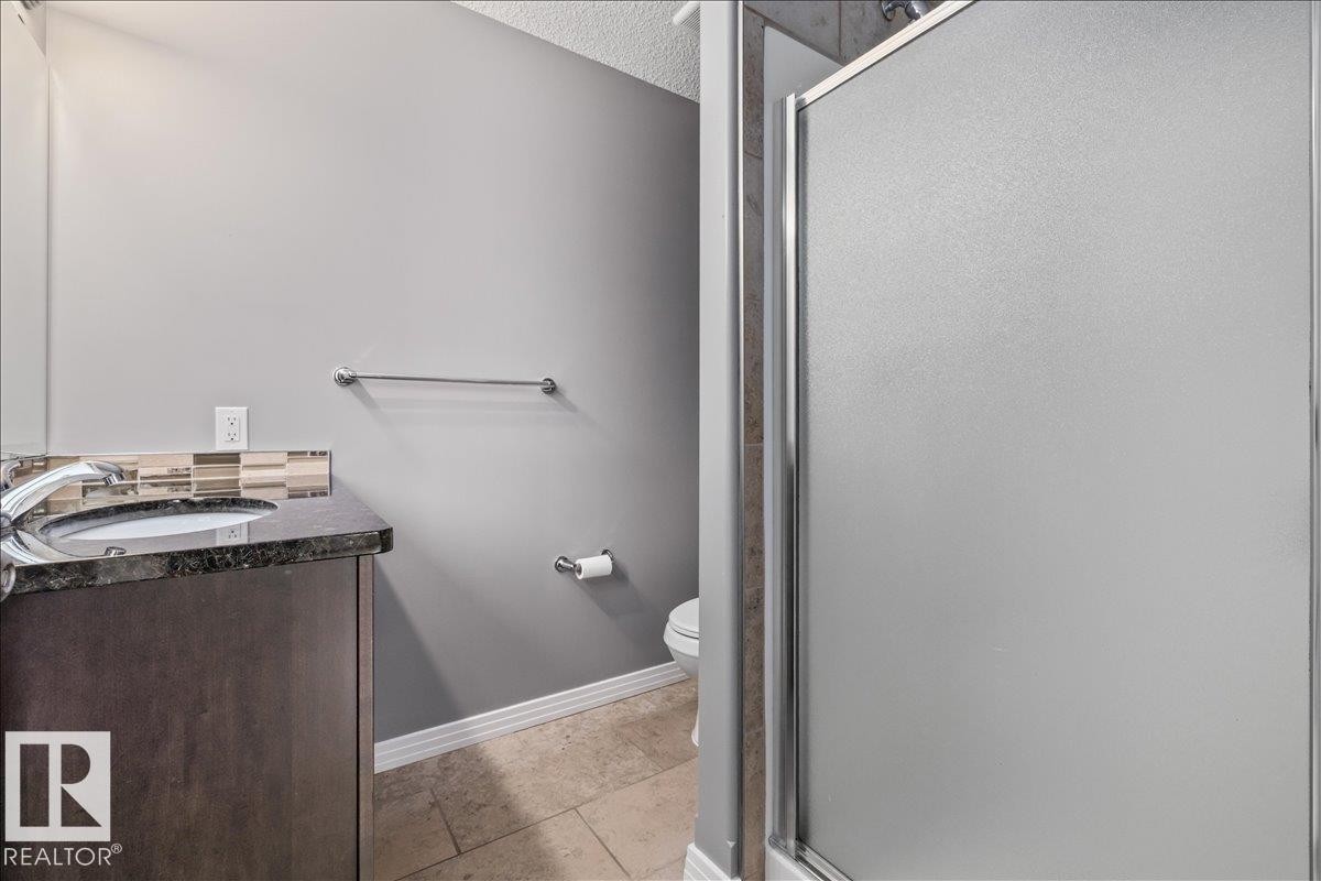 Bathroom vanity with dark wood-finish cabinetry, a polished dark countertop, and a vessel sink with a chrome faucet - 1086 Grantham Drive Nw, Edmonton, AB - Indoor Photo Showing Bathroom