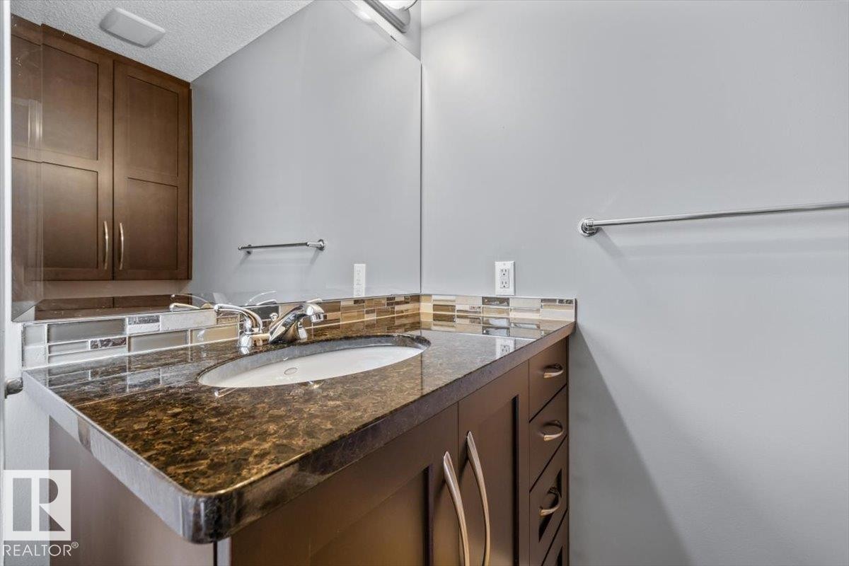 Bathroom vanity featuring a polished stone countertop with an integrated oval sink, chrome-finish faucet, and a tiled backsplash - 1086 Grantham Drive Nw, Edmonton, AB - Indoor Photo Showing Bathroom