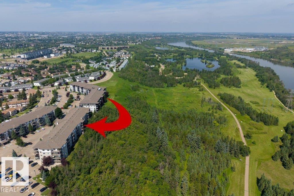 Multiple residential buildings with sloped roofs, surrounded by dense greenery, and a river in the background - #307 1188 Hyndman Rd Nw, Edmonton, AB - Outdoor With View