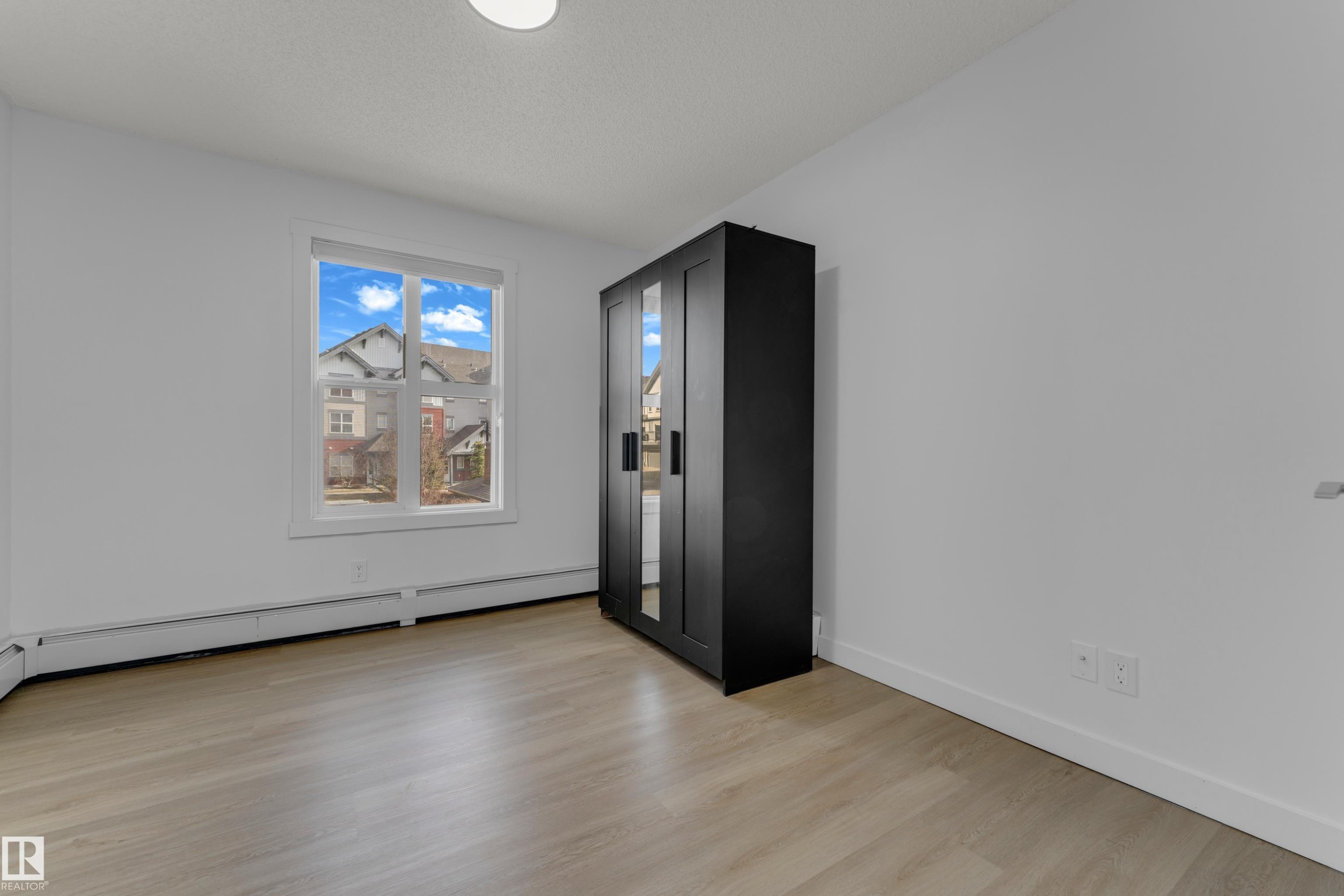 Light wood-finish flooring, white walls, and a large window providing natural light - #217 667 Watt Bv Sw, Edmonton, AB - Indoor Photo Showing Other Room
