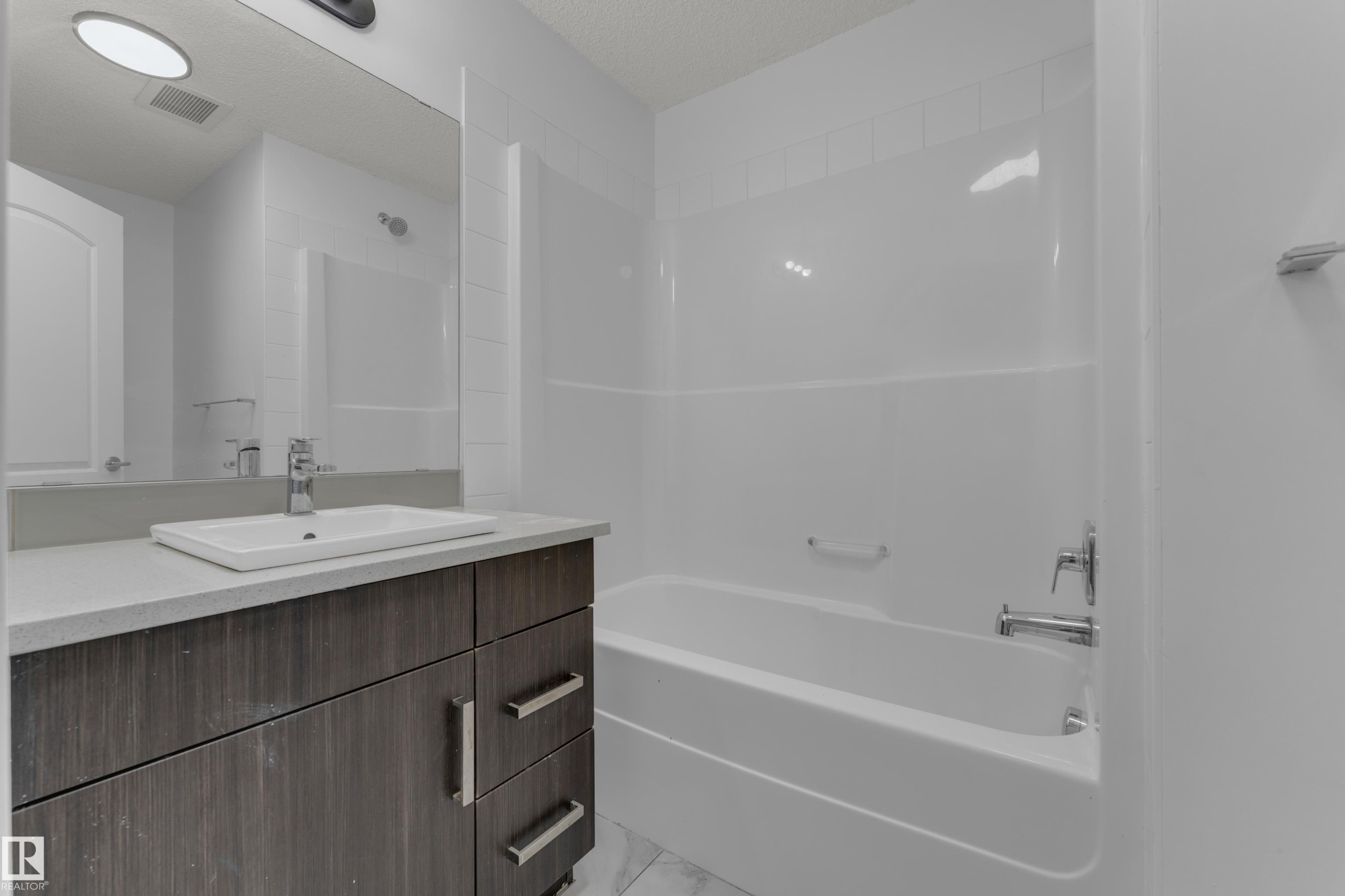Contemporary vanity with wood-finish cabinetry, light-toned countertop, and rectangular undermount sink - #217 667 Watt Bv Sw, Edmonton, AB - Indoor Photo Showing Bathroom