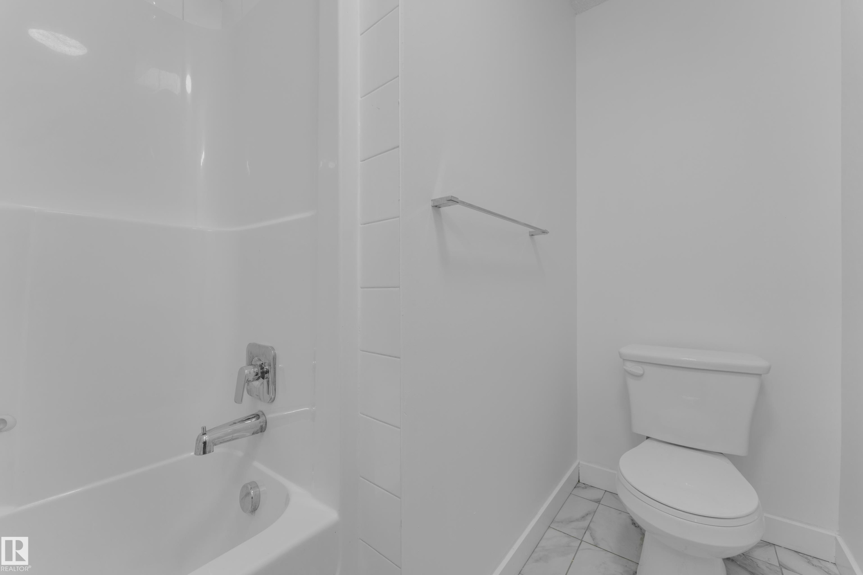 White bathtub and shower combination with chrome fixtures, white subway-style wall tile, white toilet, and patterned floor tile - #217 667 Watt Bv Sw, Edmonton, AB - Indoor Photo Showing Bathroom