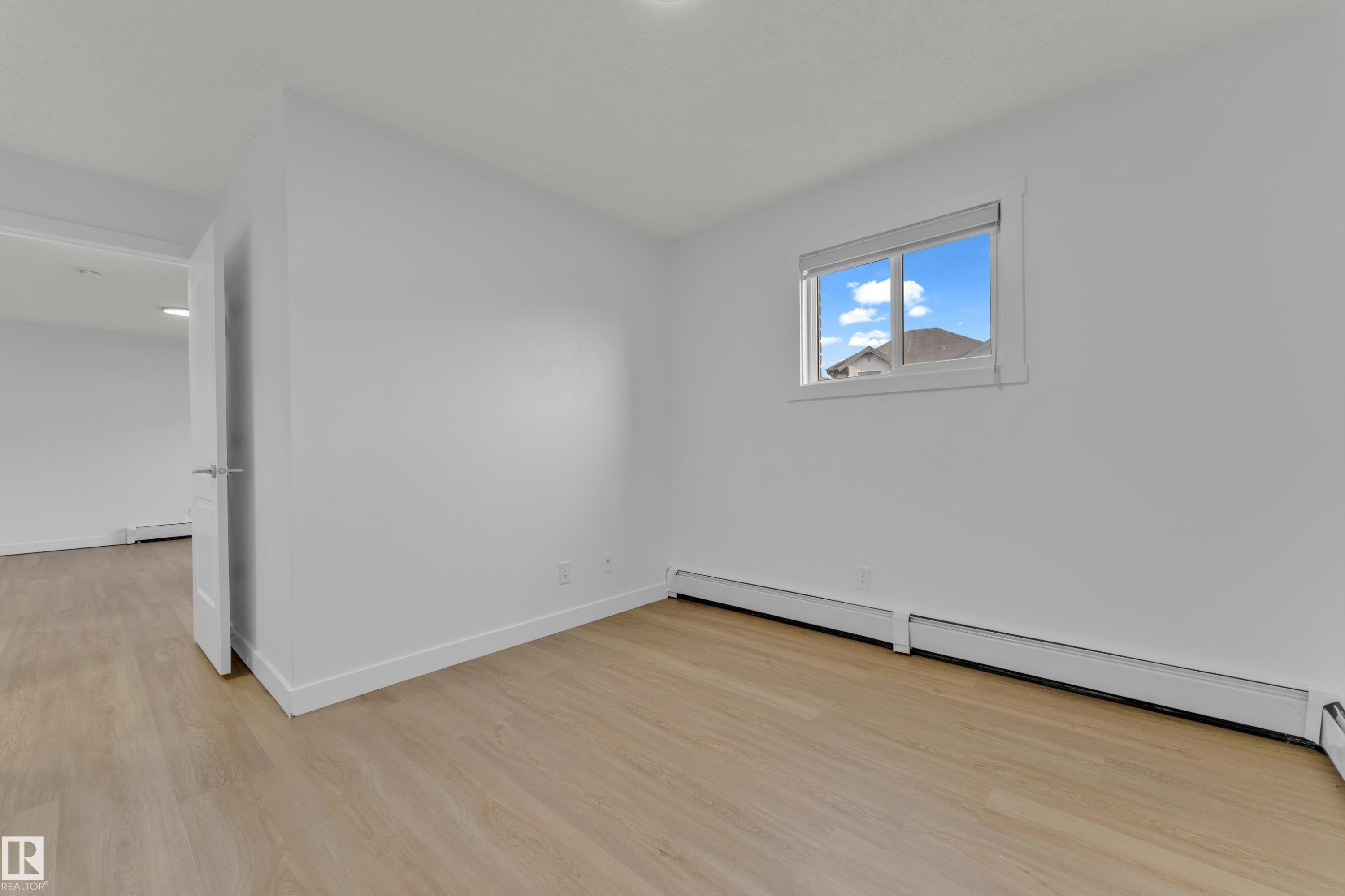 Wood-finish flooring with white baseboards, a white door frame, and a window with white trim - #217 667 Watt Bv Sw, Edmonton, AB - Indoor Photo Showing Other Room