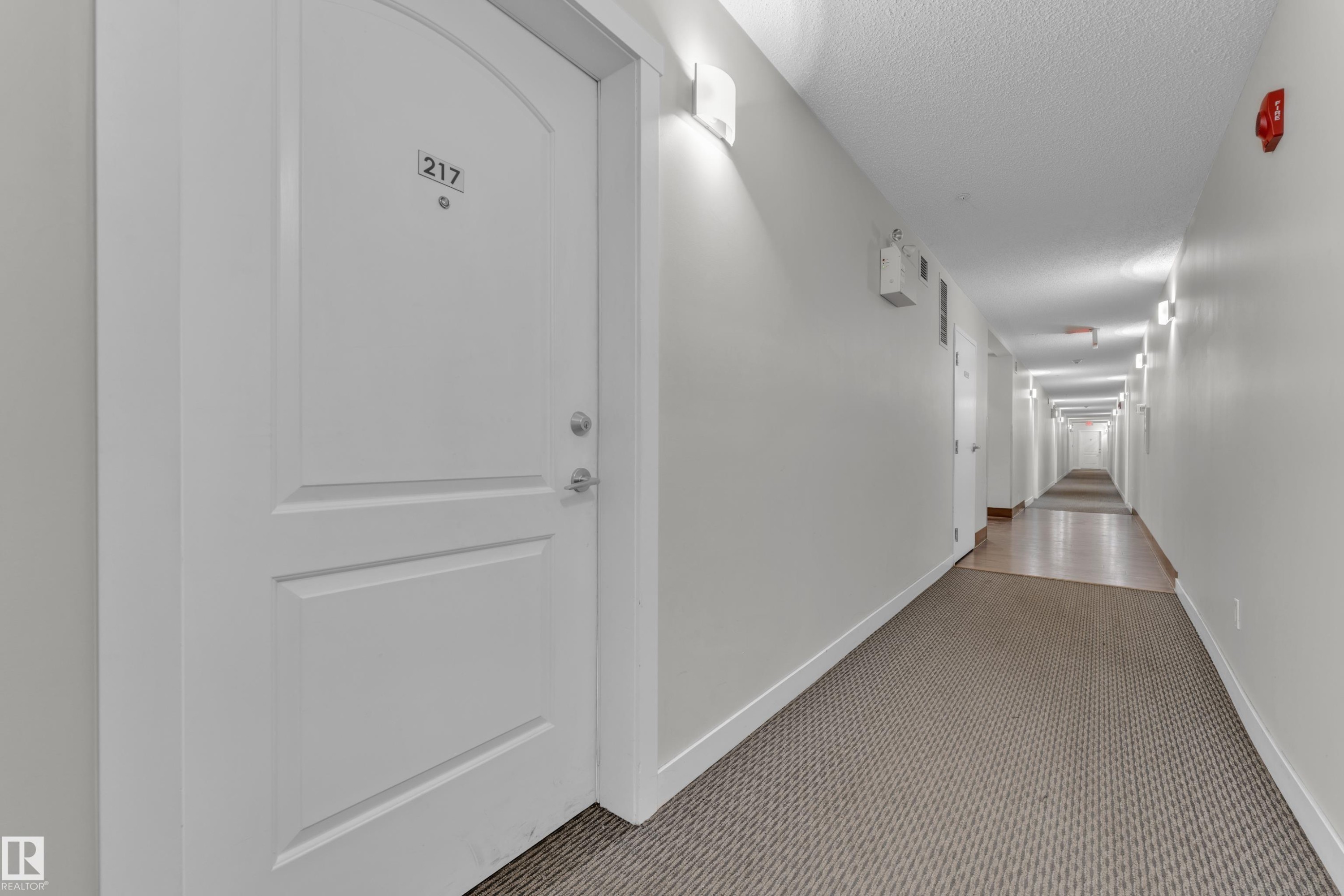 Hallway featuring textured carpeting and light-toned wall paint - #217 667 Watt Bv Sw, Edmonton, AB - Indoor Photo Showing Other Room