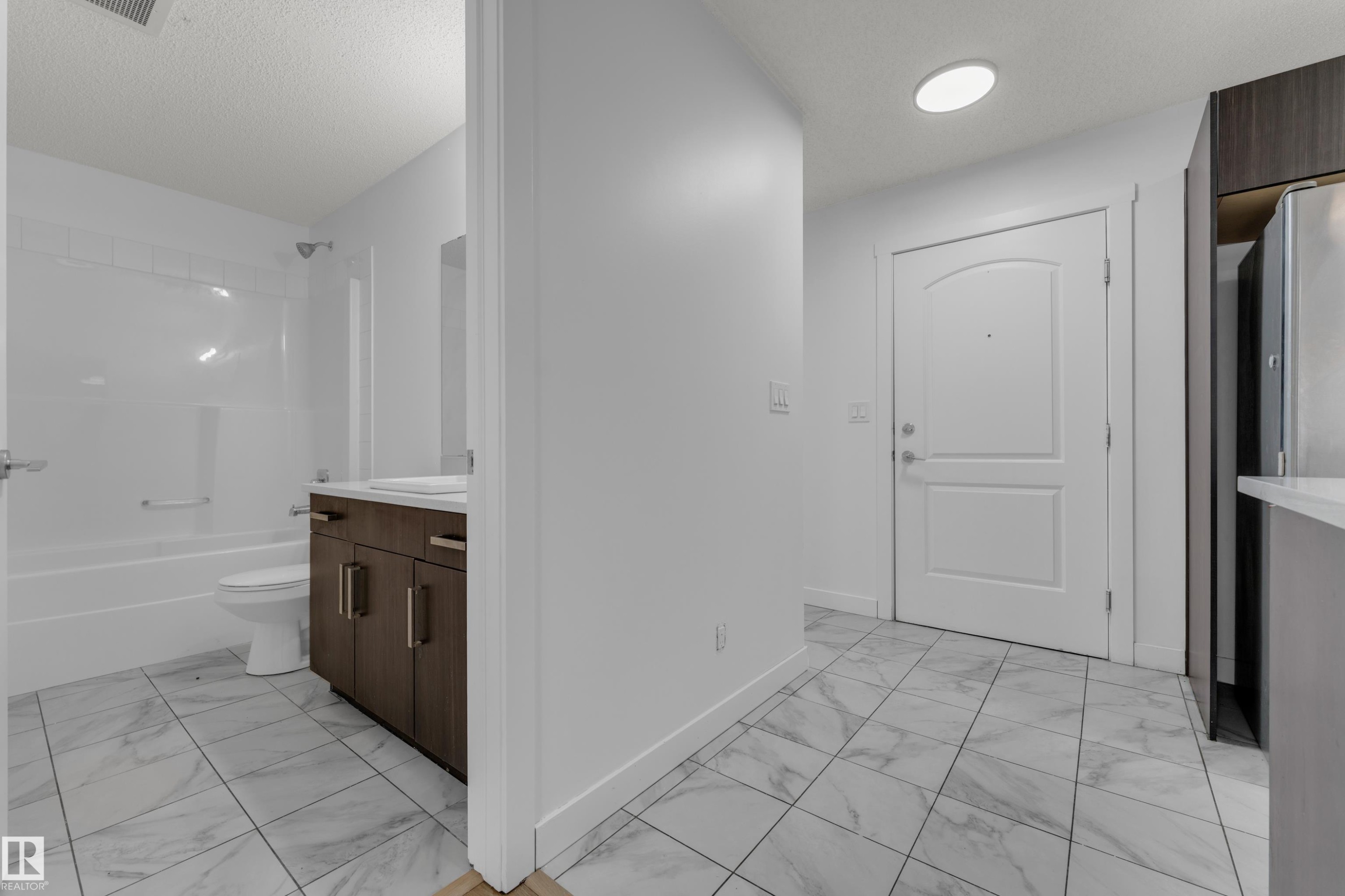 White tile flooring, white walls, and a white arched panel door create a cohesive design - #217 667 Watt Bv Sw, Edmonton, AB - Indoor Photo Showing Bathroom