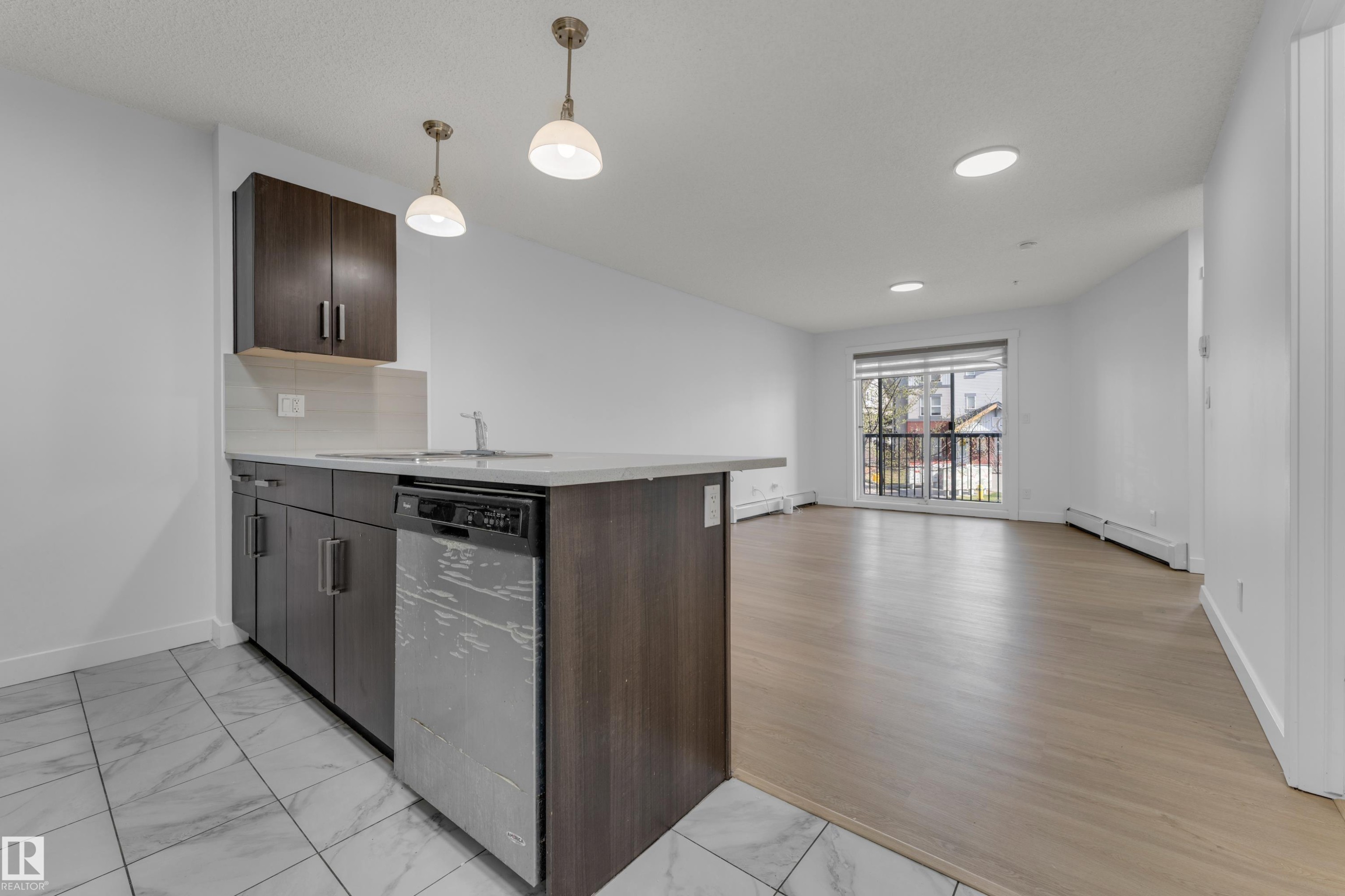 Modern kitchen featuring dark wood-finish cabinetry, light stone-finish countertops, stainless steel appliances, and pendant lighting - #217 667 Watt Bv Sw, Edmonton, AB - Indoor Photo Showing Kitchen