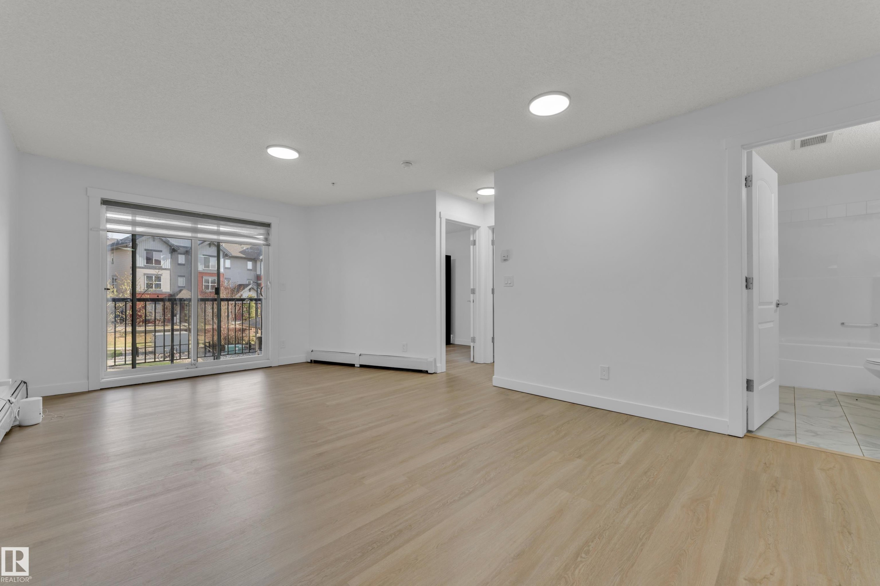 Light wood-finish flooring, white walls, recessed ceiling lighting, and a private balcony with black metal railings - #217 667 Watt Bv Sw, Edmonton, AB - Indoor Photo Showing Living Room