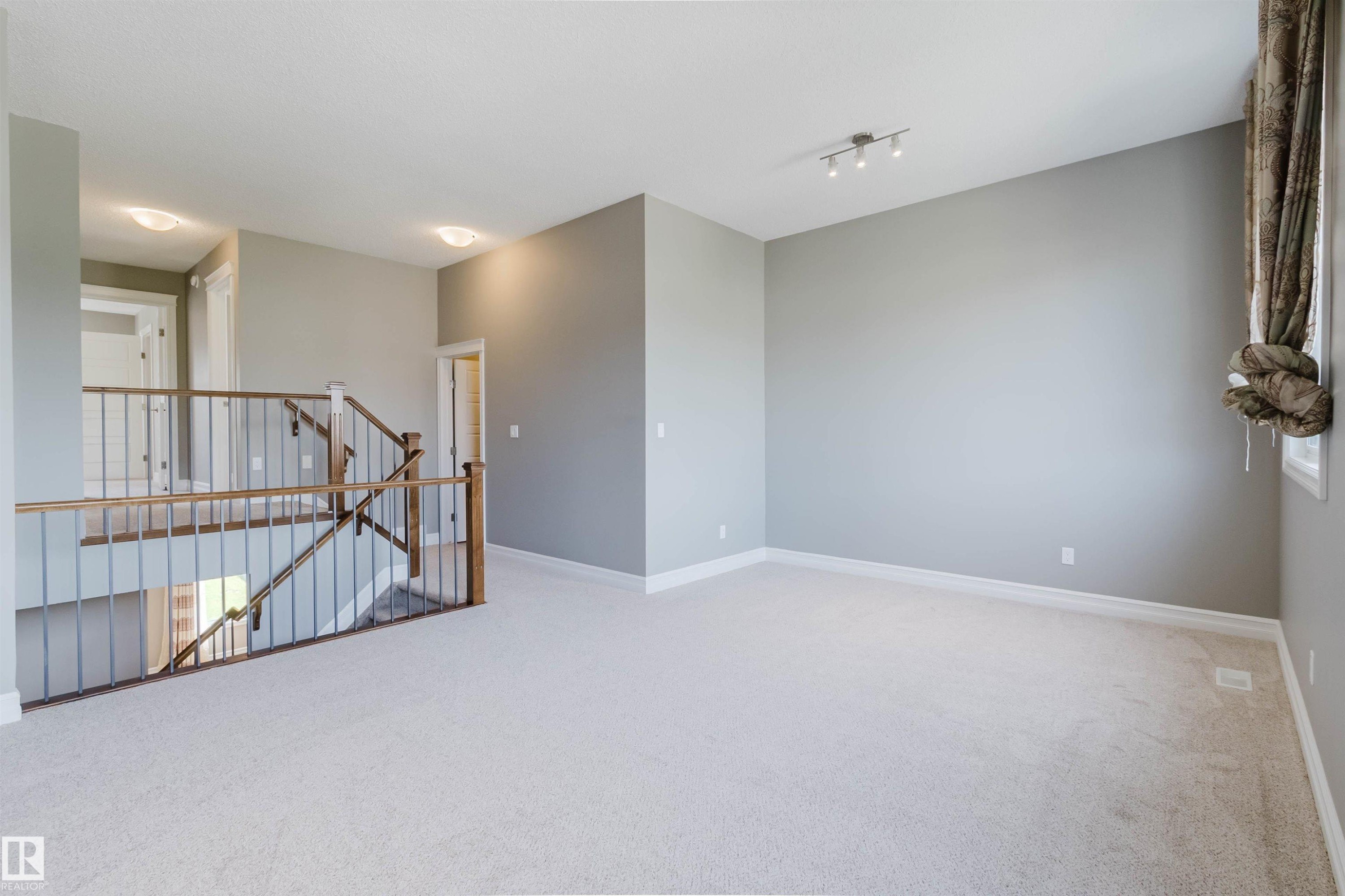Carpeted flooring, contemporary wall lighting, track lighting fixture, wood and metal staircase railing, and neutral wall tones - 15839 10 Avenue Sw, Edmonton, AB - Indoor Photo Showing Other Room