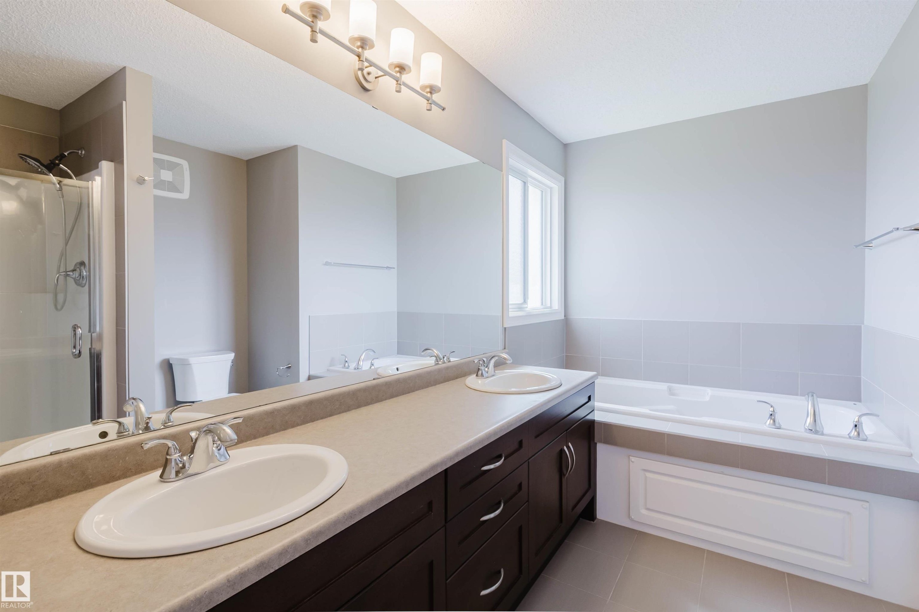 Spacious bathroom featuring a dual vanity with undermount sinks, a built-in bathtub, a window, and a glass-enclosed shower - 15839 10 Avenue Sw, Edmonton, AB - Indoor Photo Showing Bathroom