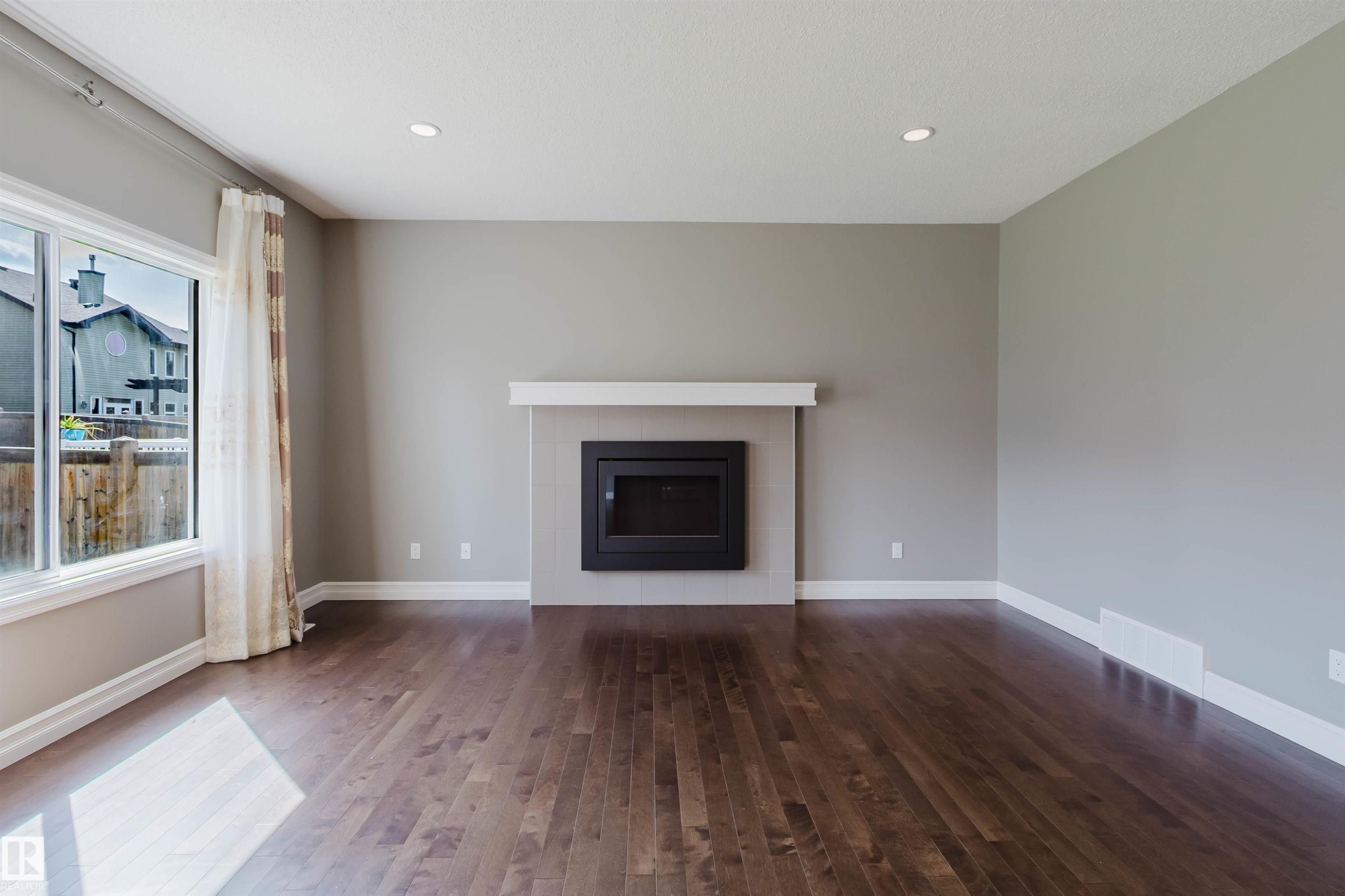 Rich wood-finish flooring, recessed lighting, and a modern fireplace with a white mantel and dark tile surround - 15839 10 Avenue Sw, Edmonton, AB - Indoor Photo Showing Living Room With Fireplace