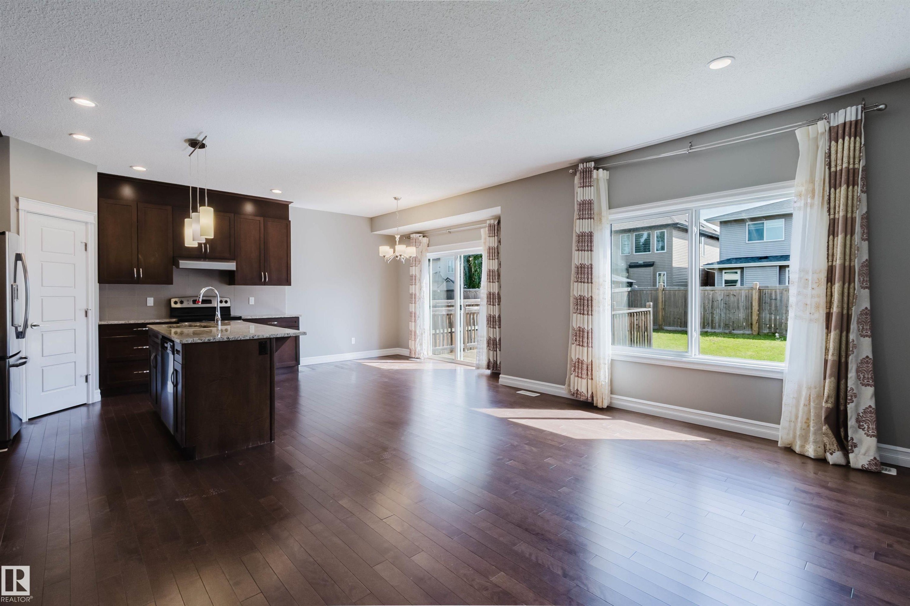 Open-concept living area featuring rich wood-finish flooring, recessed lighting, and a kitchen island with stone countertops - 15839 10 Avenue Sw, Edmonton, AB - Indoor Photo Showing Other Room