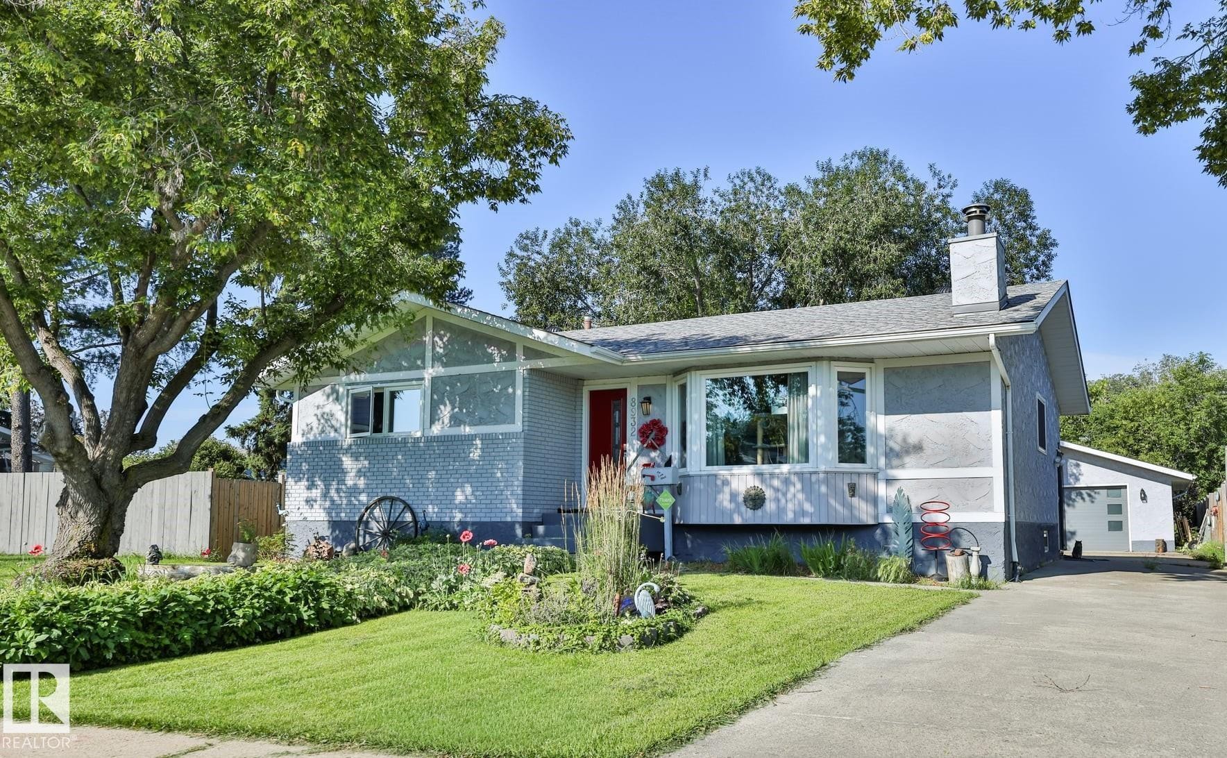 Stucco exterior with a pitched roof, front garden landscaping, a concrete driveway, and a detached garage - 8932 187 Street Nw, Edmonton, AB - Outdoor