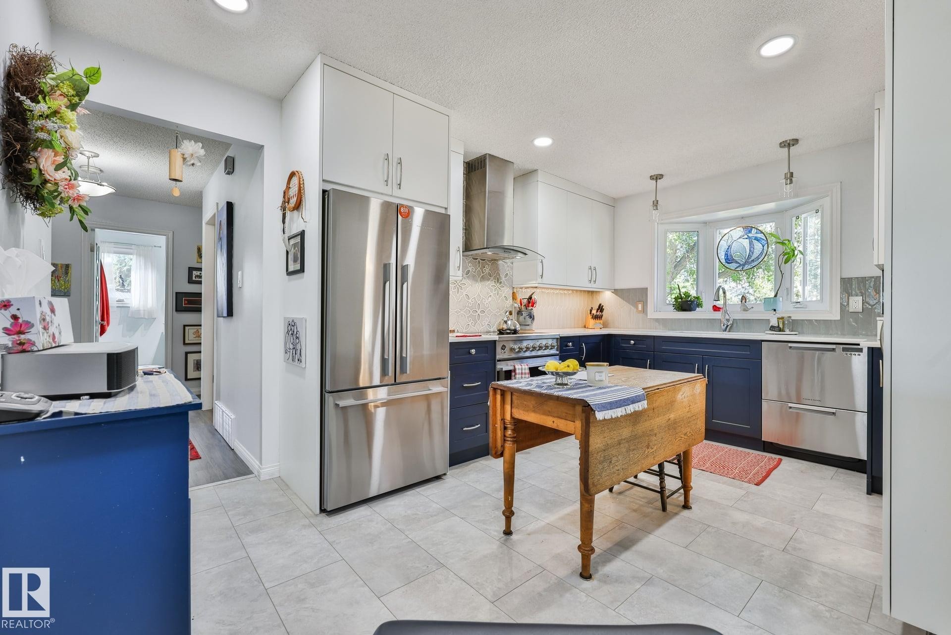 Contemporary kitchen featuring light-toned flooring, stainless steel appliances, a bay window, two-tone cabinetry, and recessed lighting - 8932 187 Street Nw, Edmonton, AB - Indoor Photo Showing Kitchen With Double Sink