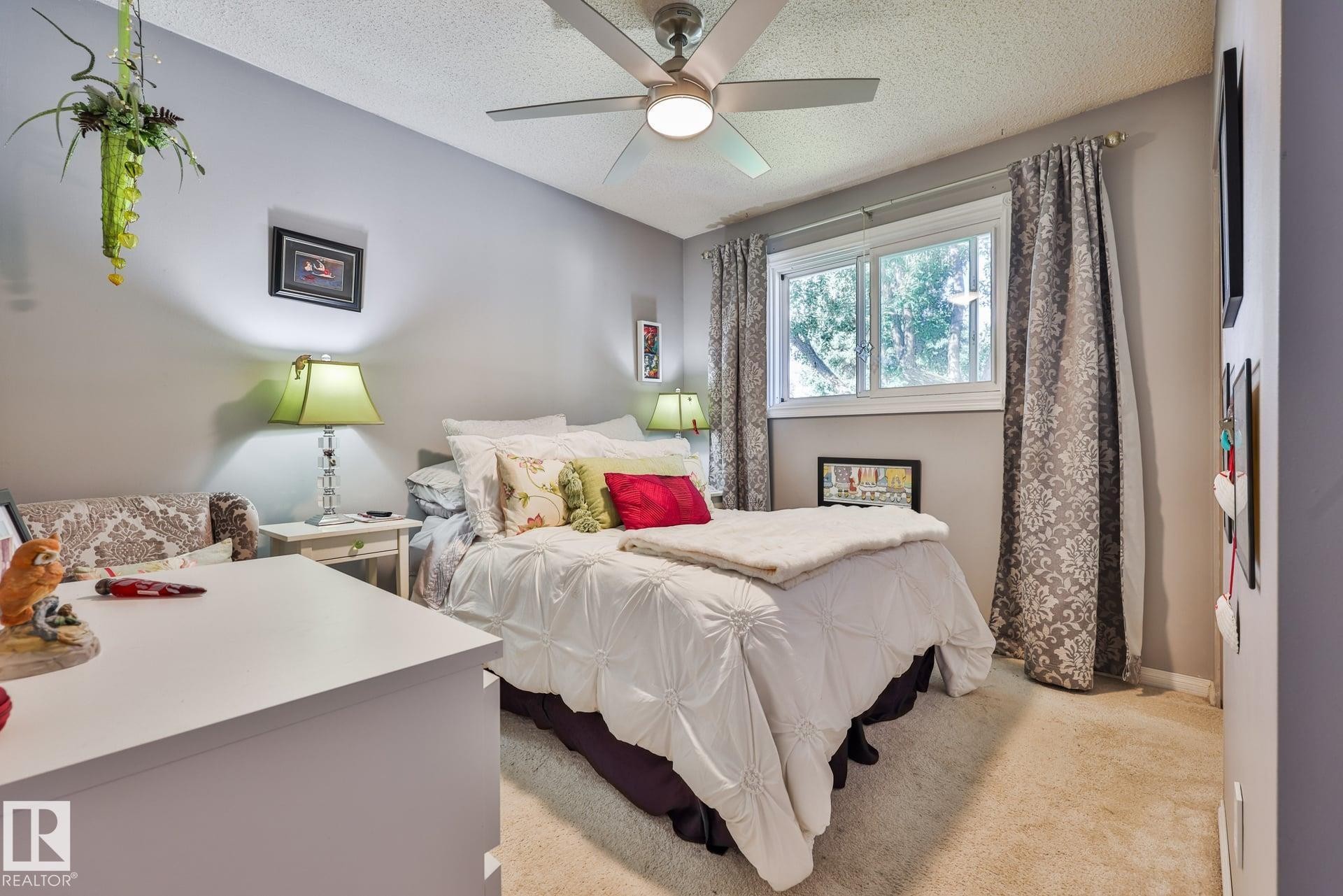 Ceiling fan with integrated lighting, window with white frame, patterned drapes, carpeted flooring, and neutral wall color - 8932 187 Street Nw, Edmonton, AB - Indoor Photo Showing Bedroom