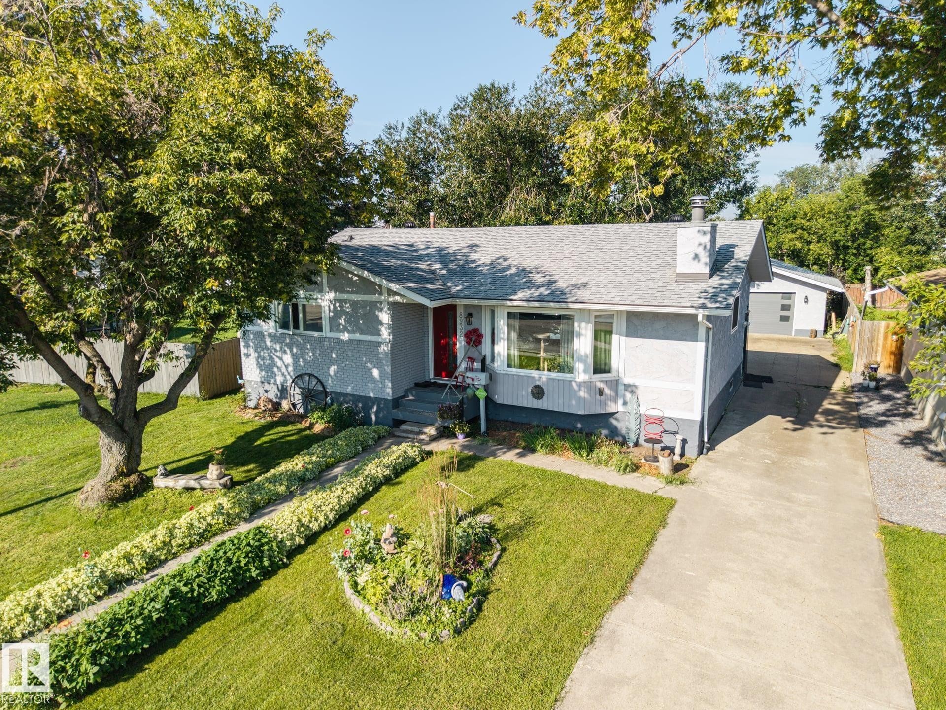 Exterior featuring a gray stucco finish, a red entry door, a prominent front window, and a concrete driveway - 8932 187 Street Nw, Edmonton, AB - Outdoor