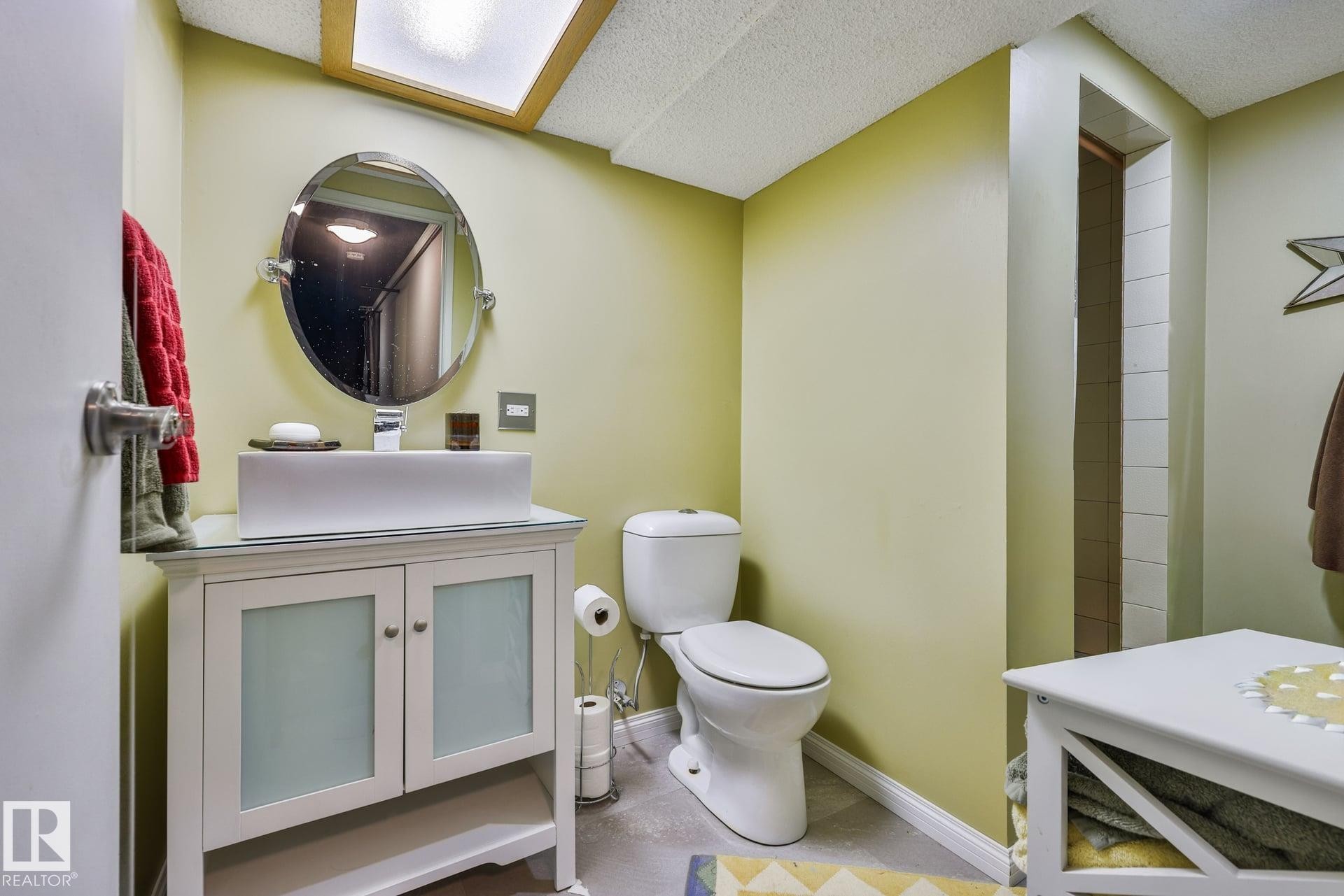 Vanity with opaque glass-front cabinetry, vessel sink, and an oval mirror - 8932 187 Street Nw, Edmonton, AB - Indoor Photo Showing Bathroom